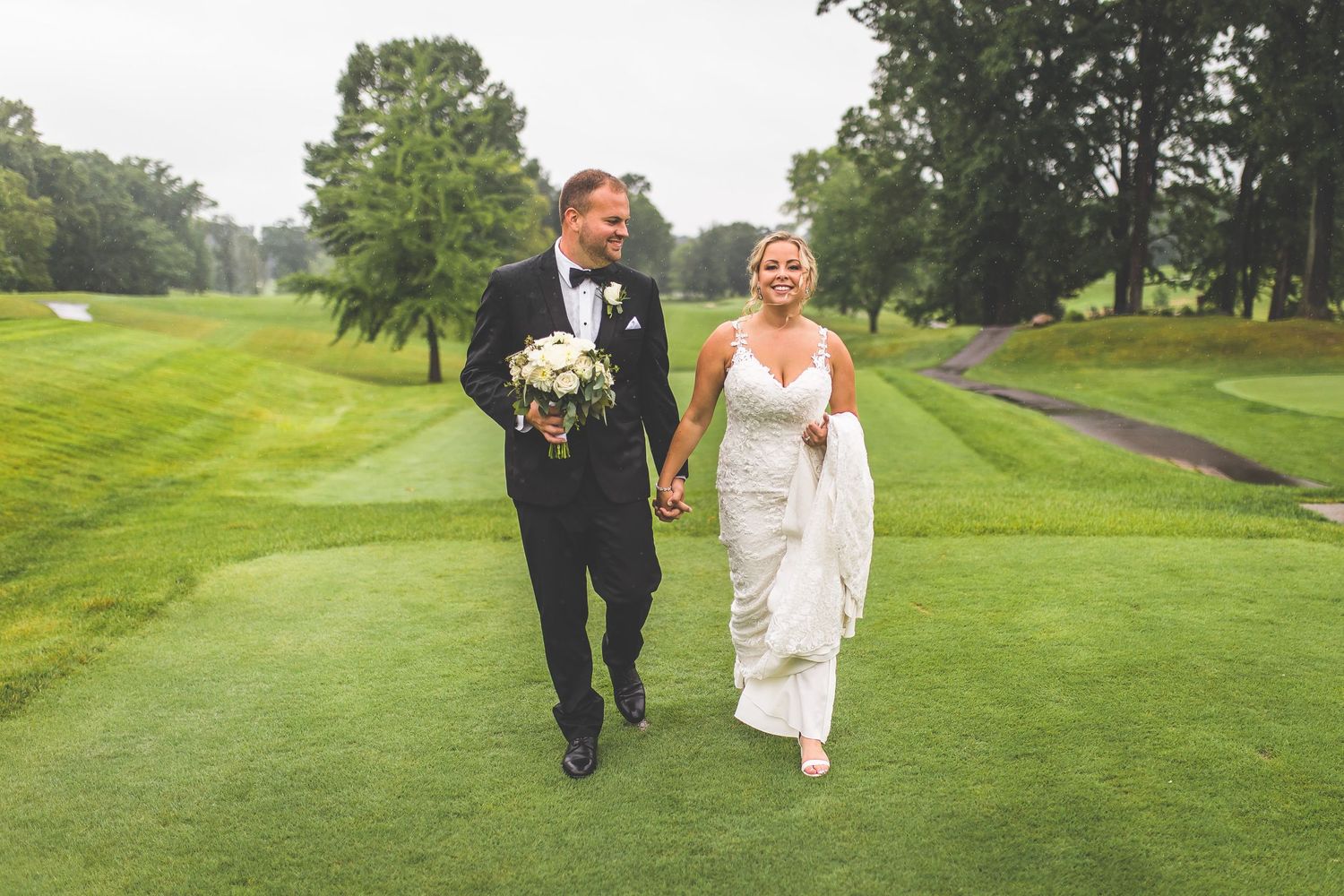 Bride and groom stroll together on manicured golf course path.
