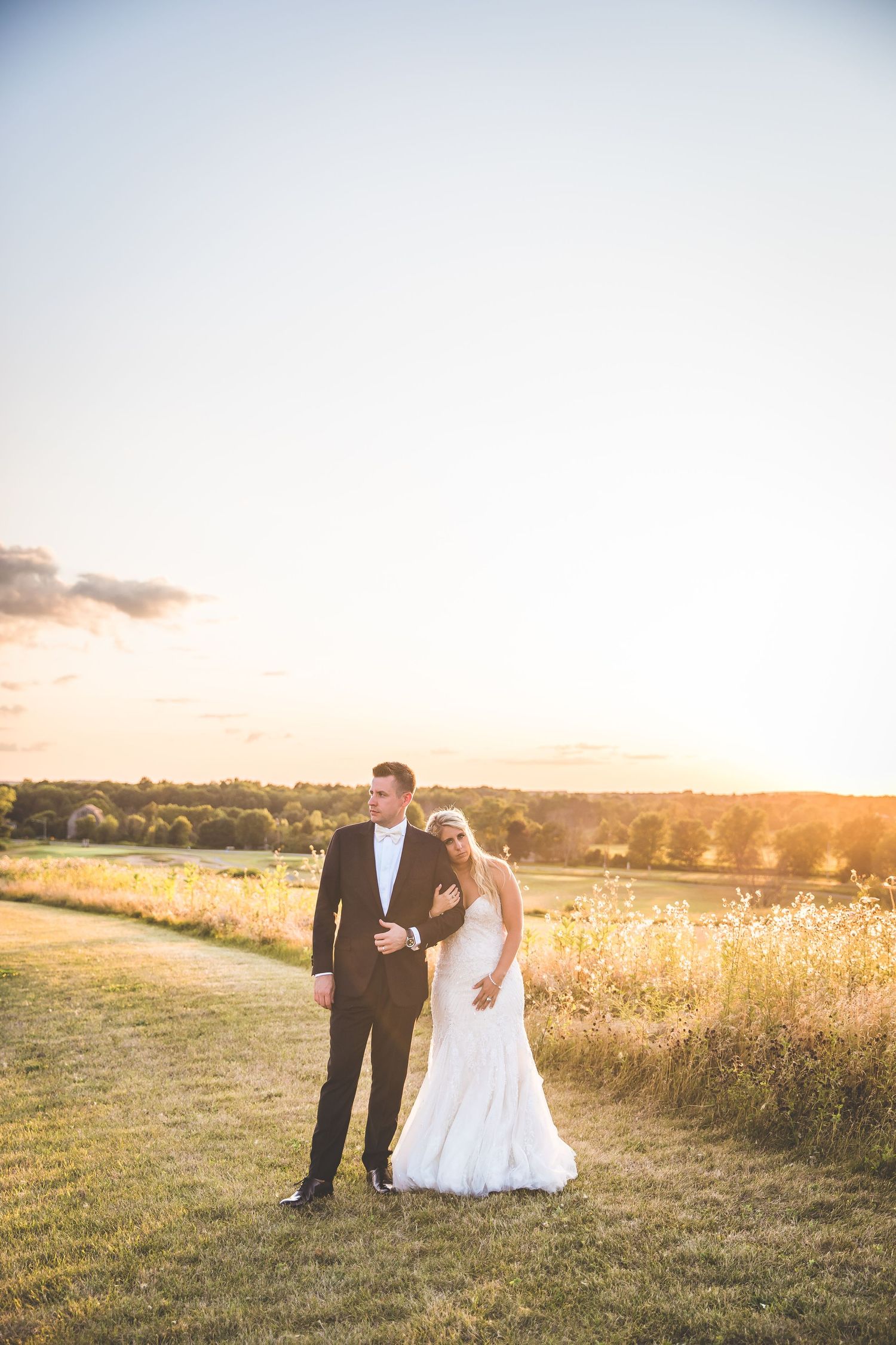 Romantic sunset photo session in a golden field with flowing white dress and formal attire.