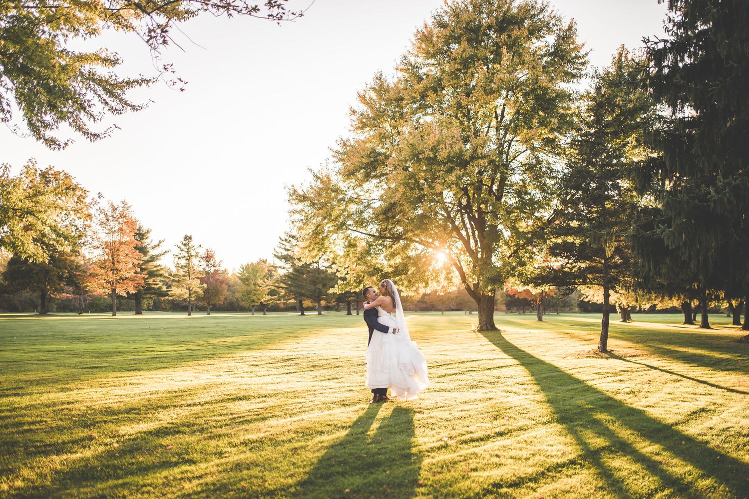 Couple walks across sunlit lawn with dramatic golden hour lighting and long shadows.