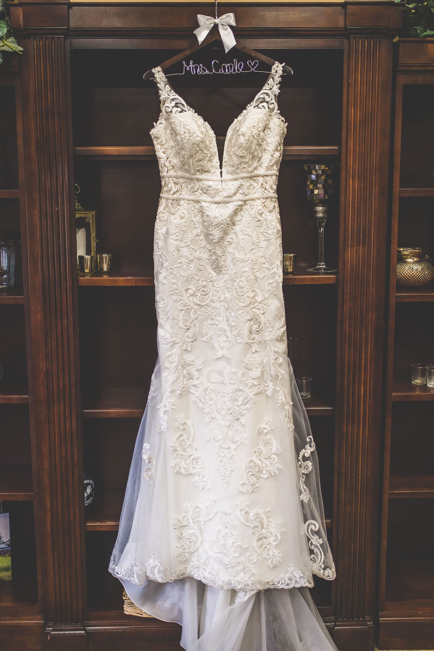 Beautiful lace wedding dress hangs on display against dark wood paneled walls.