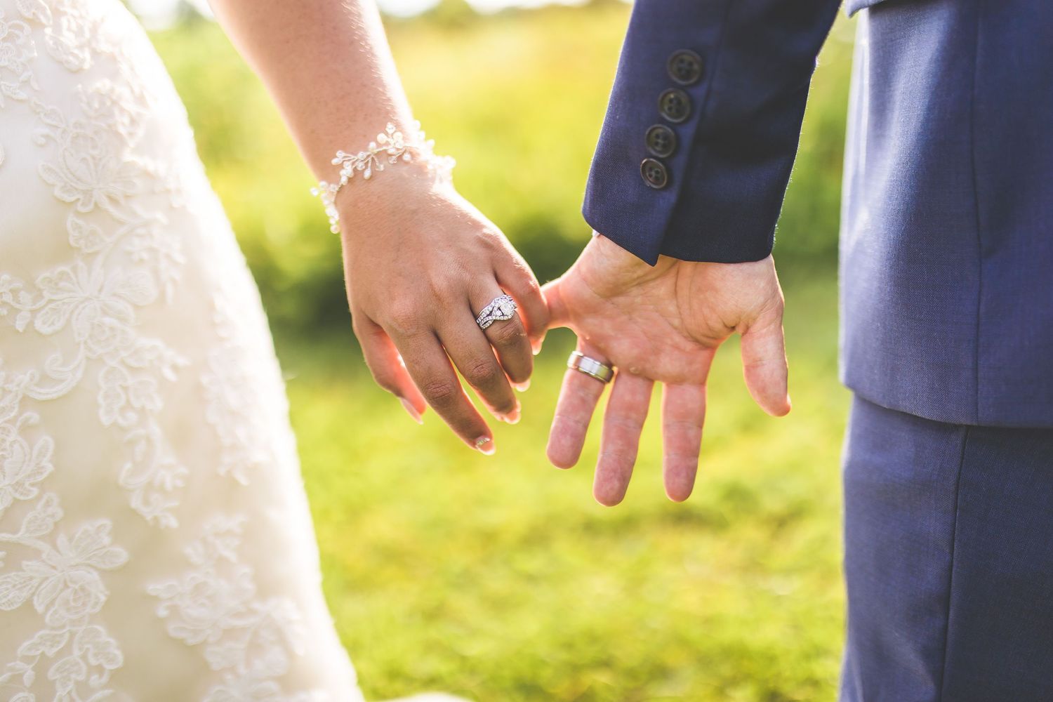 Close-up of hands wearing wedding rings against a sunlit outdoor background.