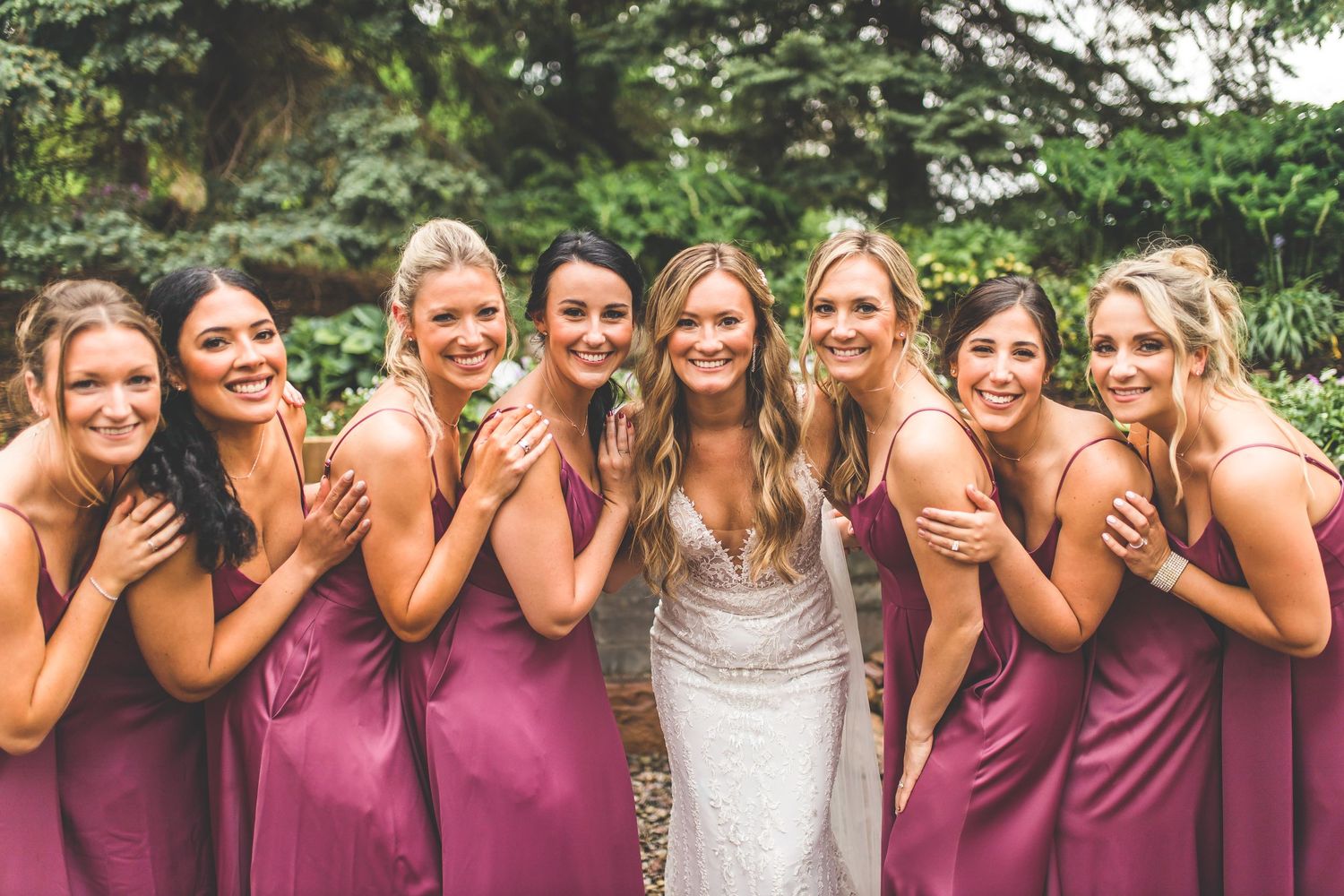 Joyful bridesmaids in matching rose dresses sharing a candid laughing moment with bride.
