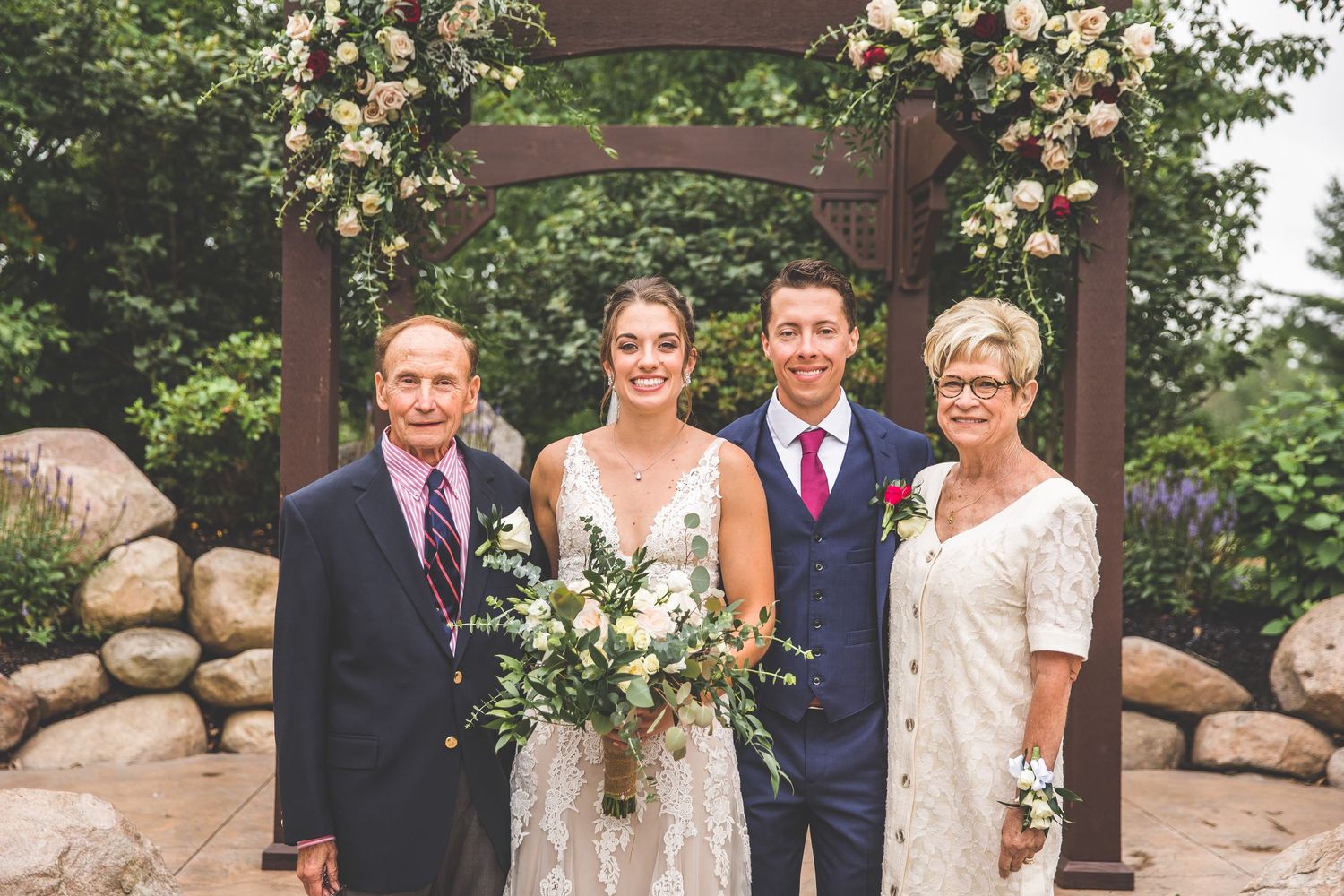 Wedding party poses under wooden pergola decorated with peach and cream flowers.