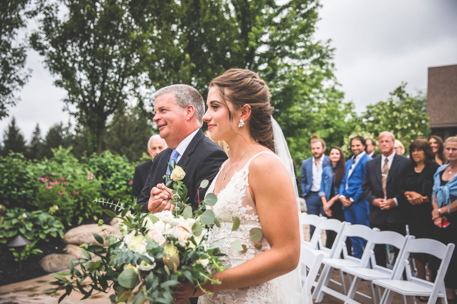 Wedding ceremony in progress at an outdoor venue with lush green trees in the background.