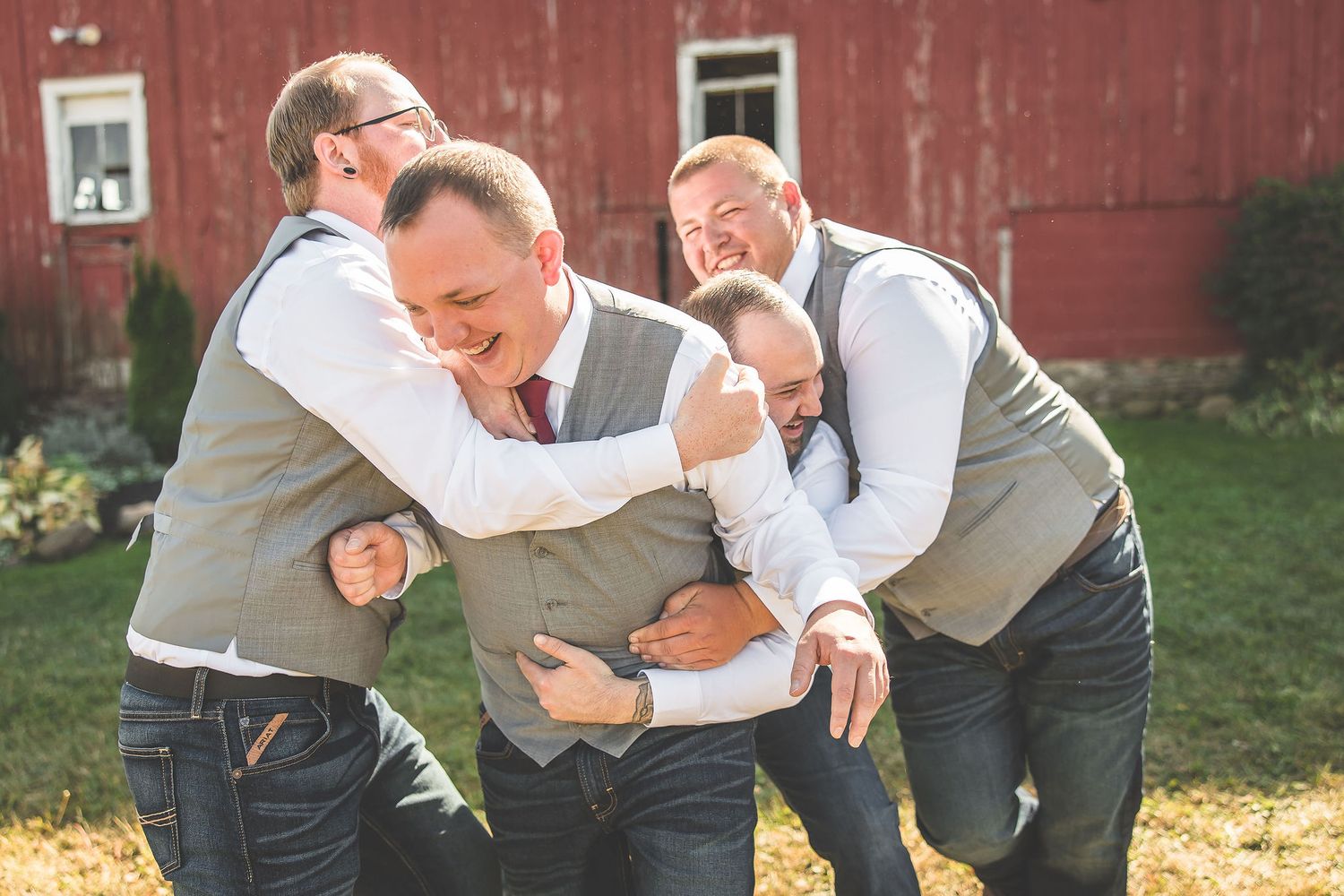 Wedding party poses playfully in front of a rustic red barn on a sunny autumn day.