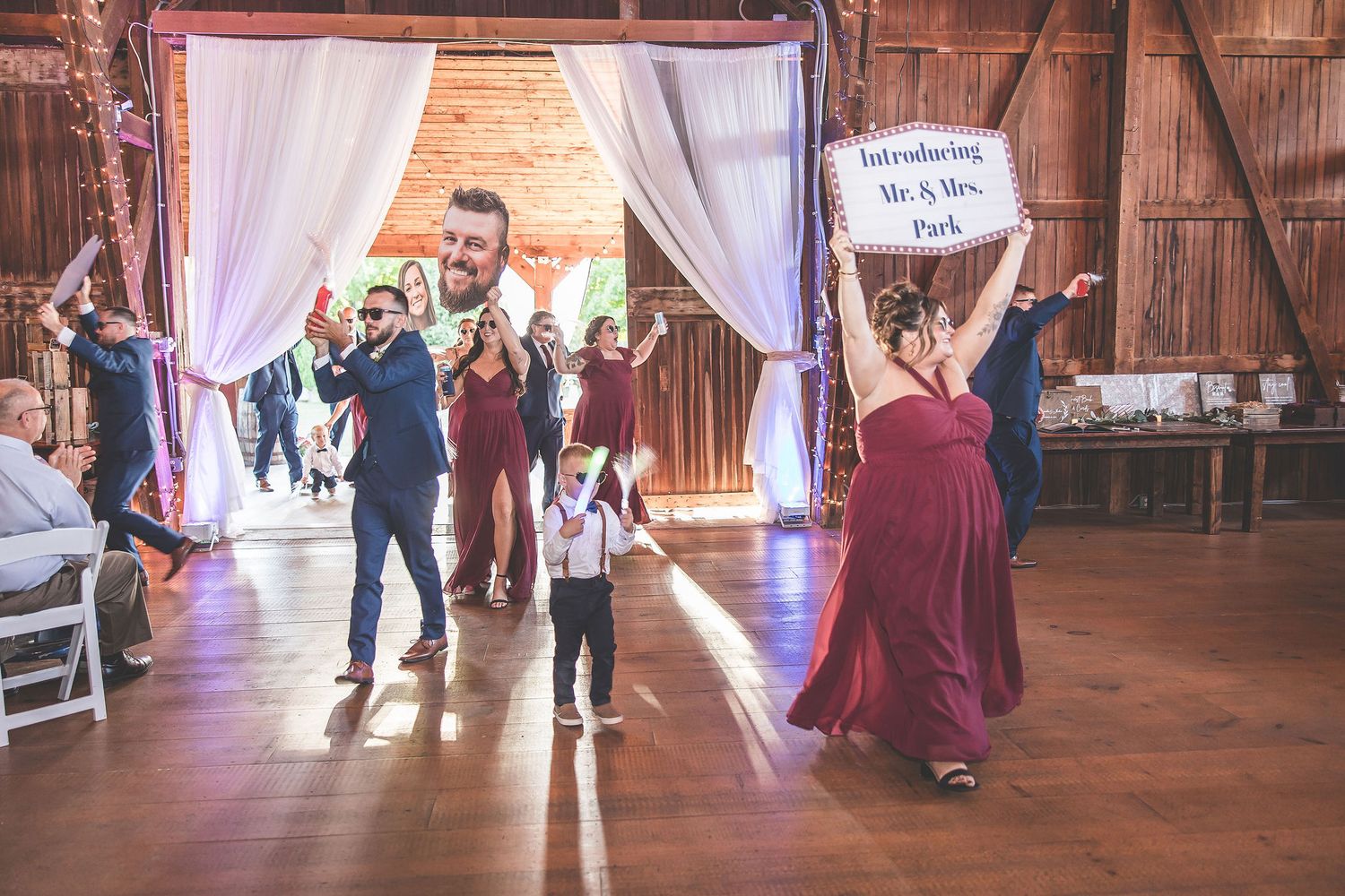 Wedding party dancing in rustic barn venue with white drapes and purple uplighting creating romantic atmosphere.