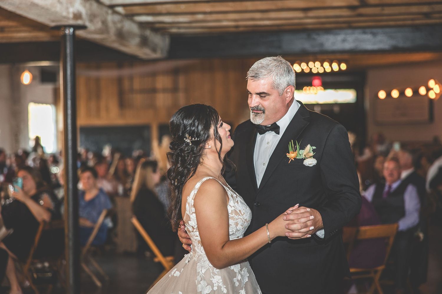 Wedding guests dancing and celebrating in rustic barn venue with string lights.