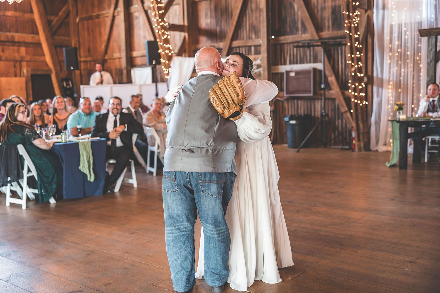 Couples dancing on wooden floor during barn wedding reception with string light decorations.