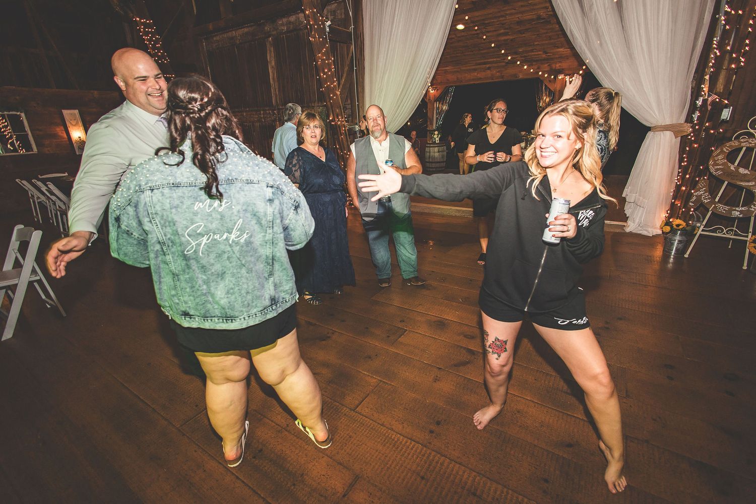 Wedding reception guests dancing and celebrating on a wooden dance floor at an indoor venue.