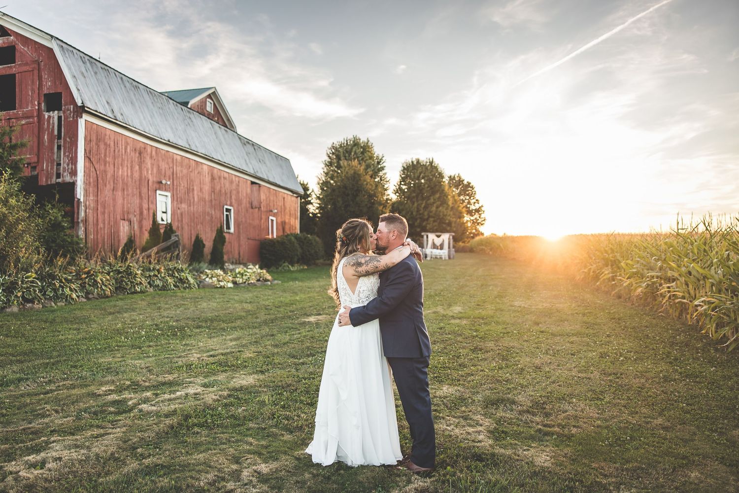 Romantic sunset portraits of a wedding couple posing in front of a rustic red barn.
