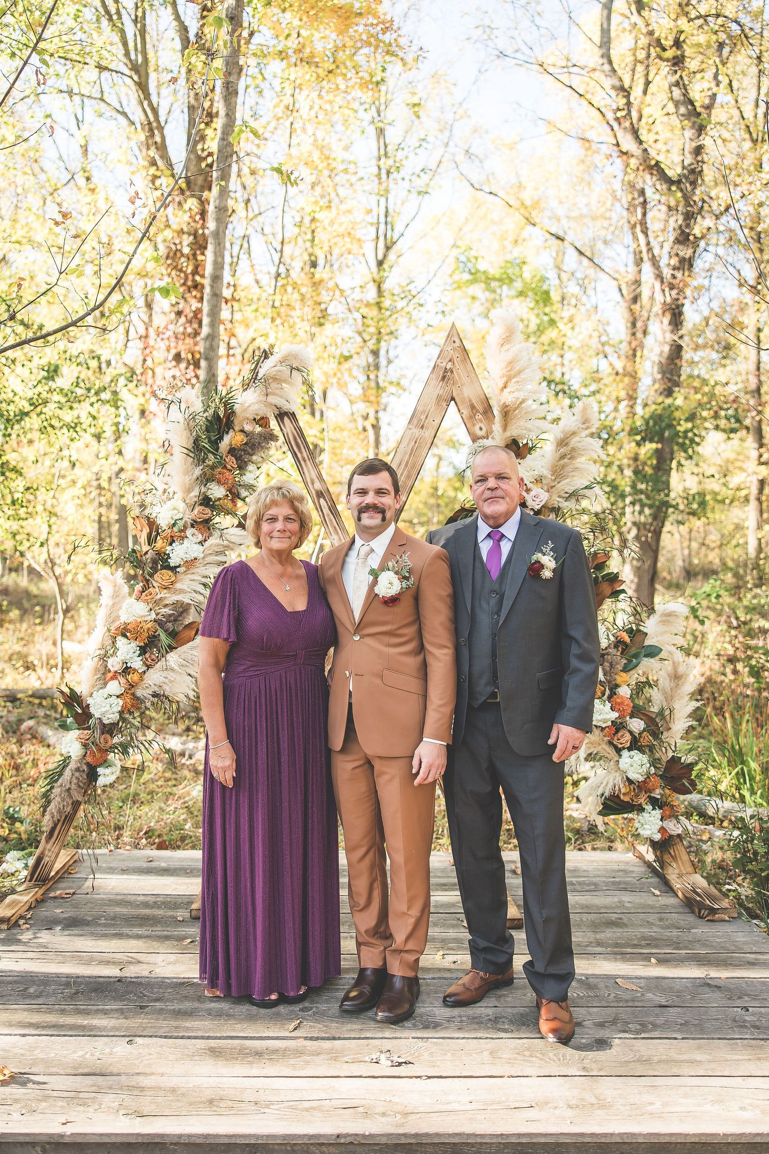 Wedding party members stand in pairs along a woodland path during fall season.