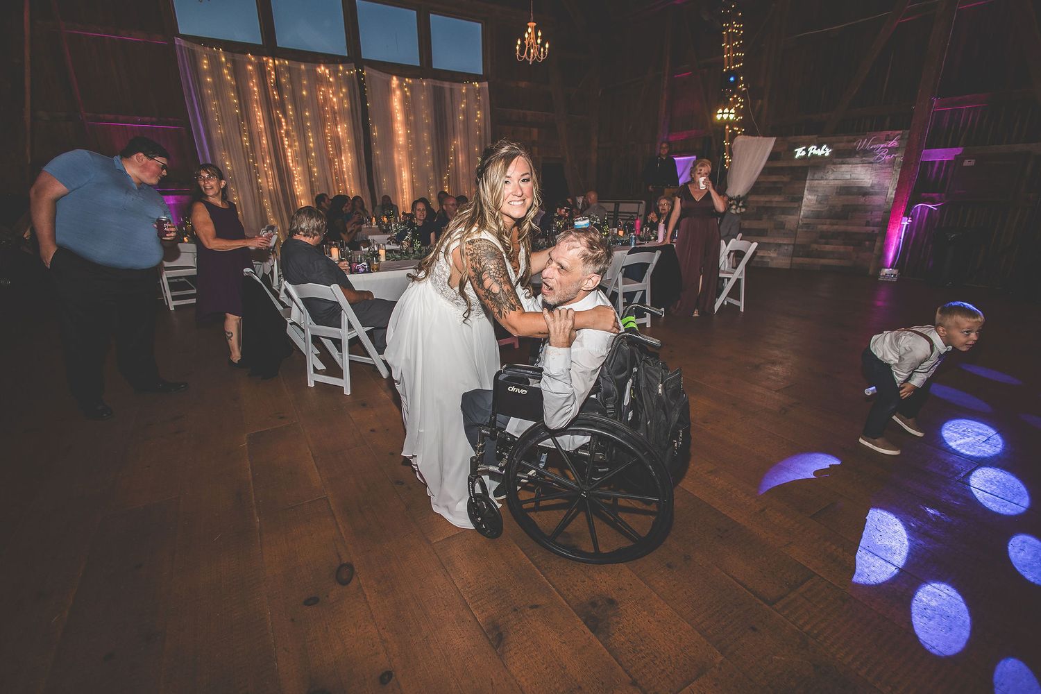 Wedding guests dancing and celebrating on the dance floor with purple lighting effects.