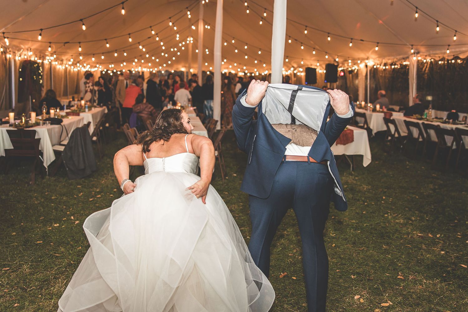 Elegant wedding reception under a tent with twinkling lights and dancing guests.