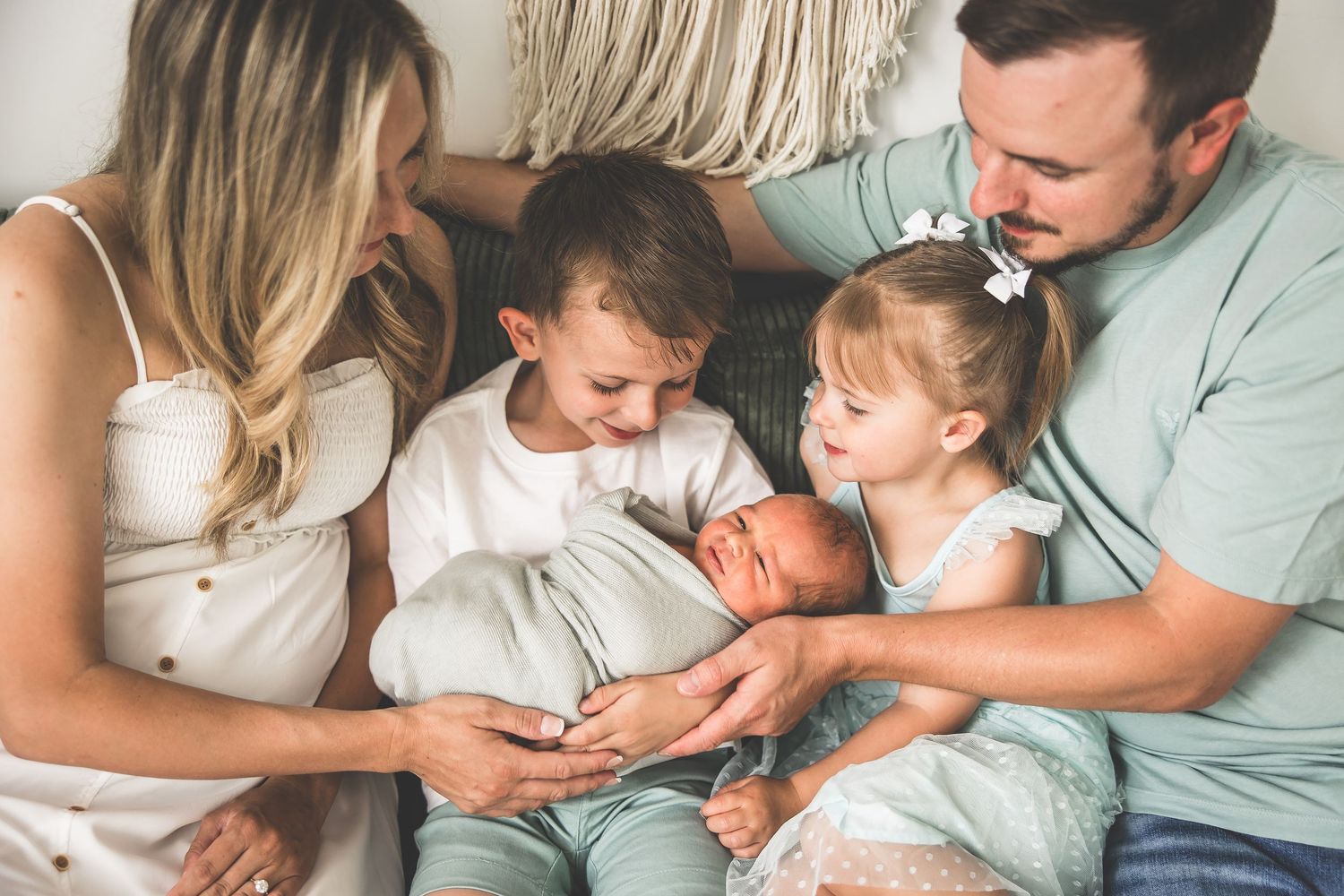 A family gathers on a couch to welcome their newborn baby in an intimate moment.