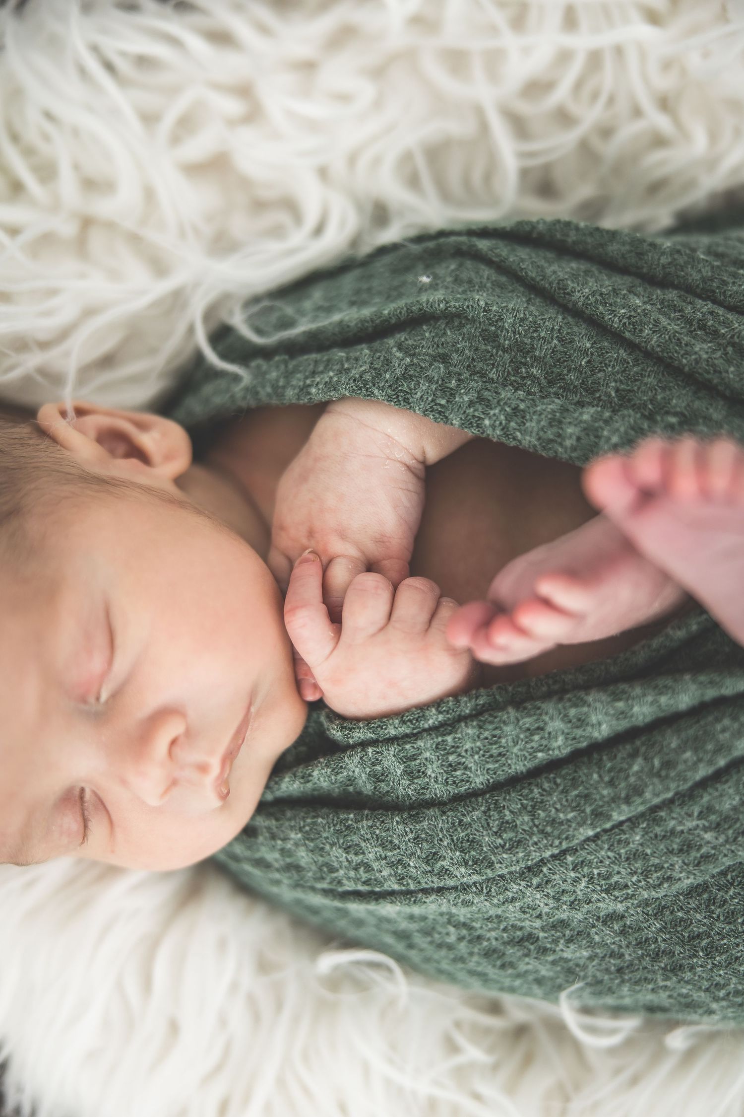 Sleeping newborn wrapped in green knit blanket on white textured background.