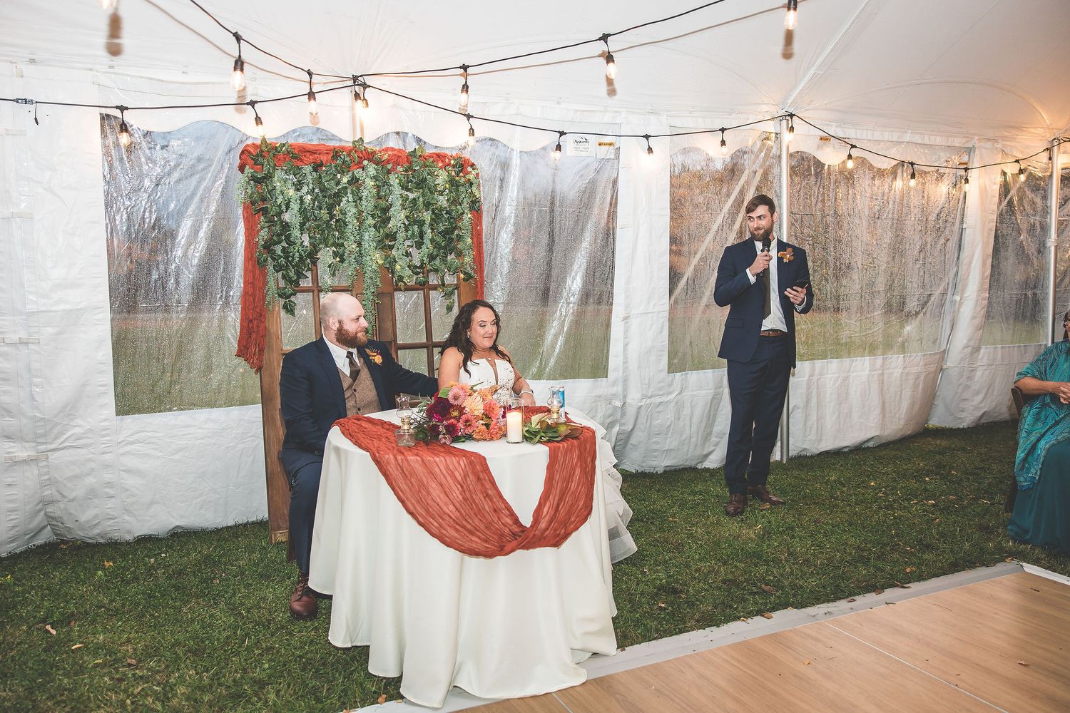 Wedding reception tent decorated with string lights and white drapes creating an elegant atmosphere.