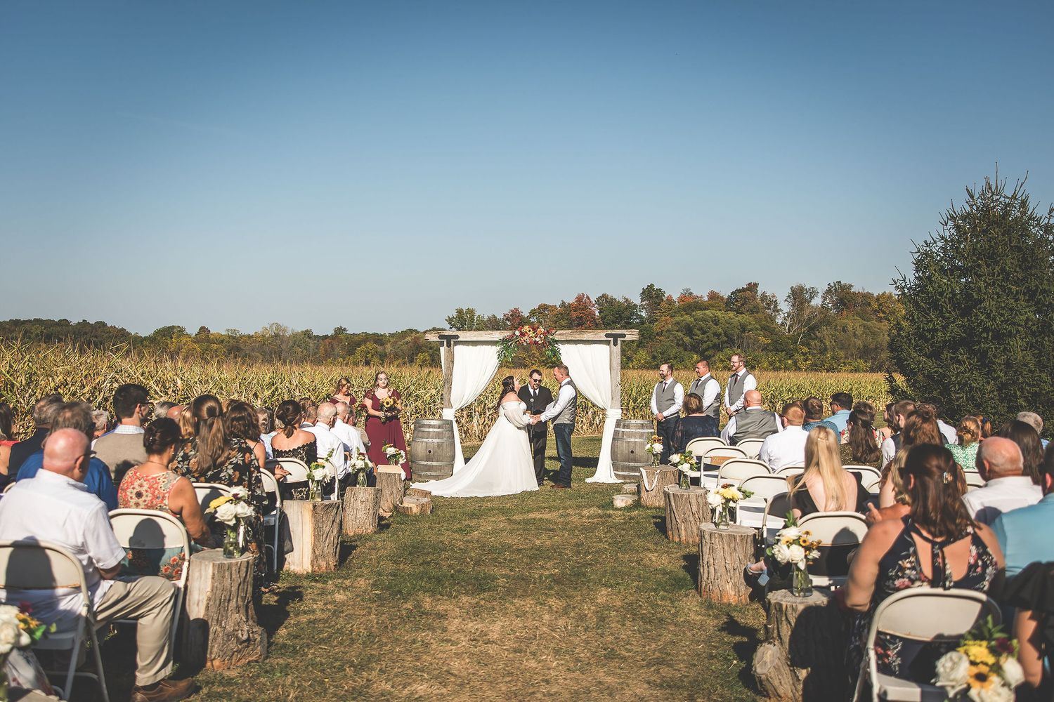Wide angle view of outdoor wedding ceremony with guests gathered on hillside.