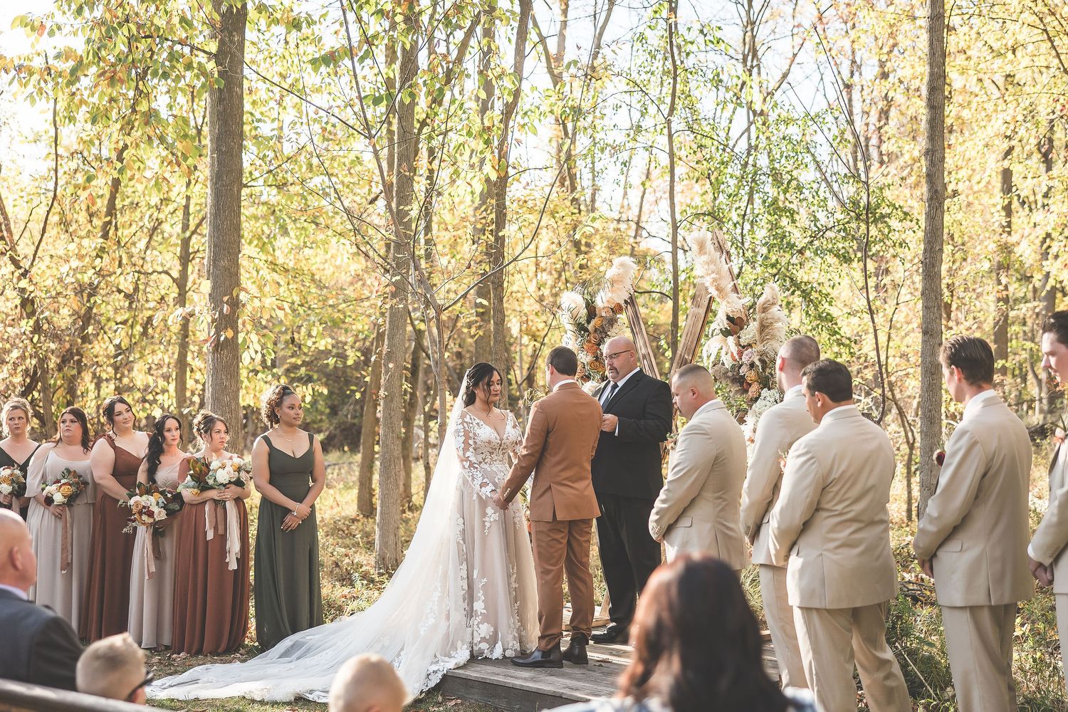 Wedding guests gathered in wooded outdoor ceremony space during fall season.
