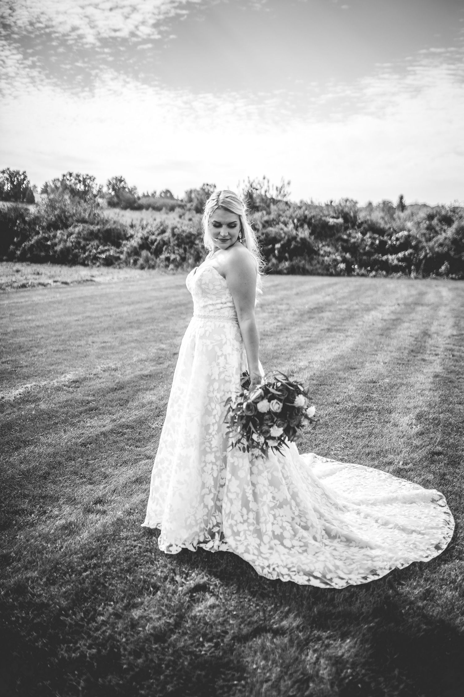 A stunning lace wedding dress with a flowing train photographed in a garden setting.