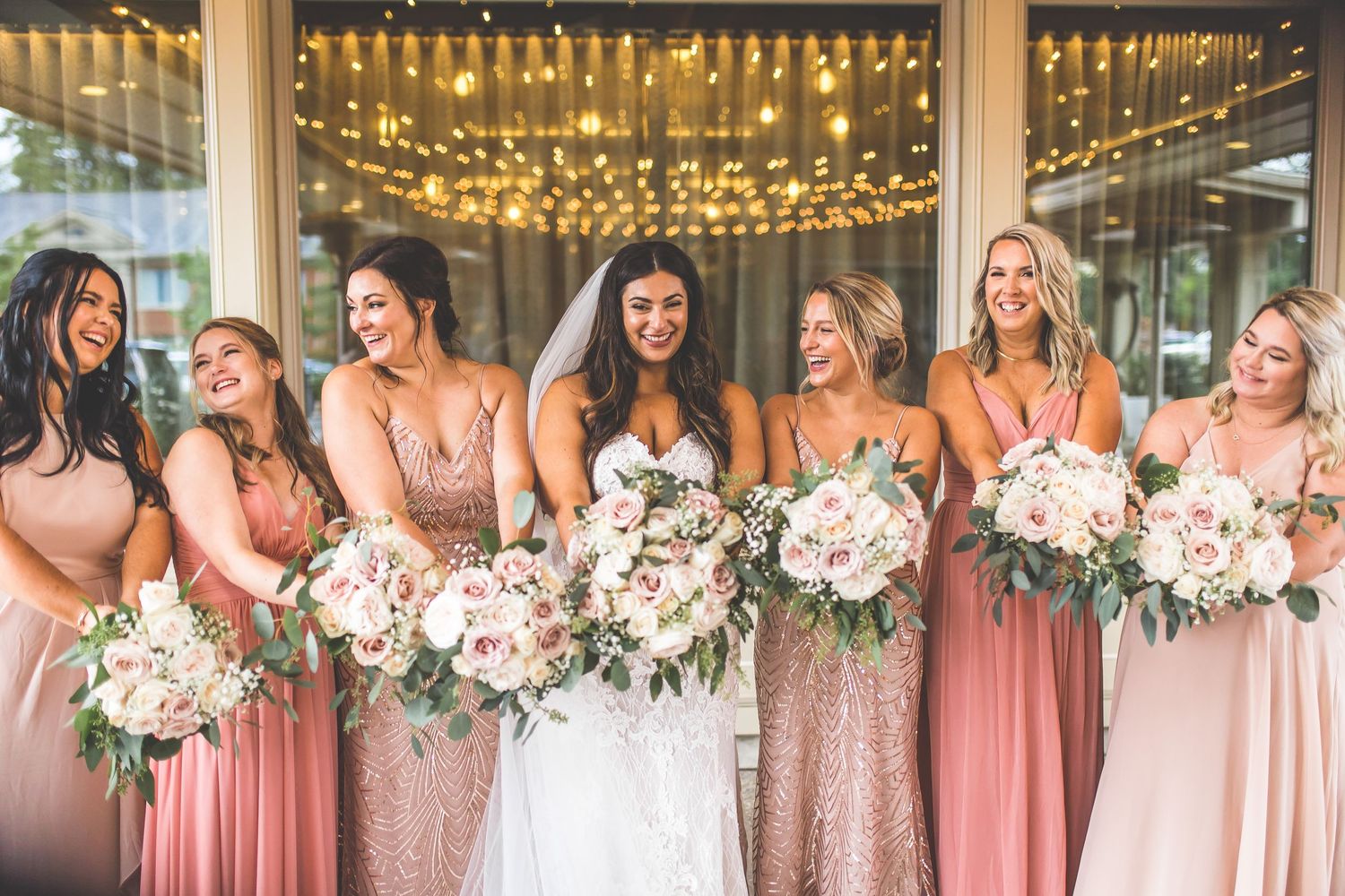 Wedding party stands in line under twinkling lights wearing pink and white dresses.