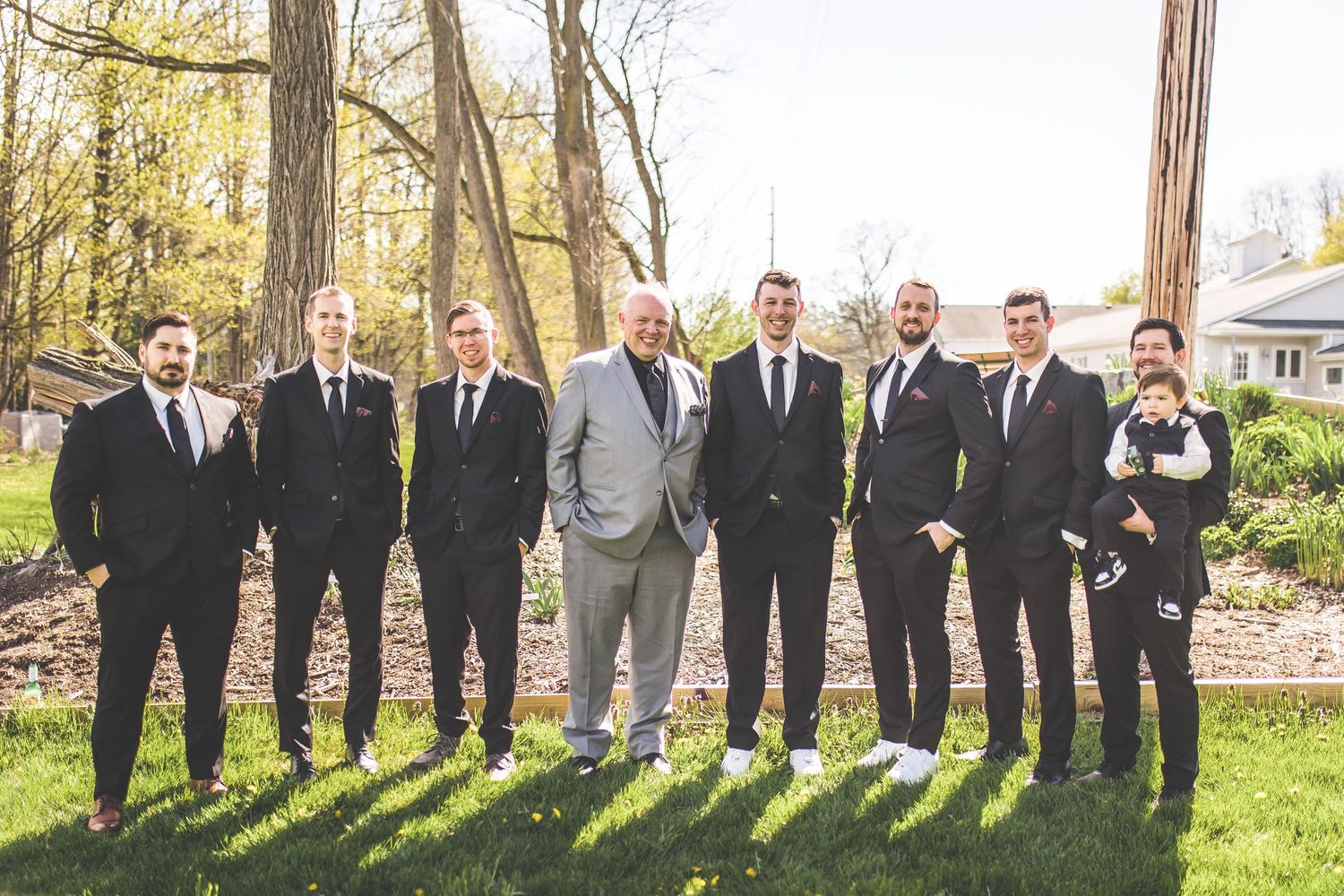 Wedding party in formal attire casting long shadows on grass during outdoor photo session.