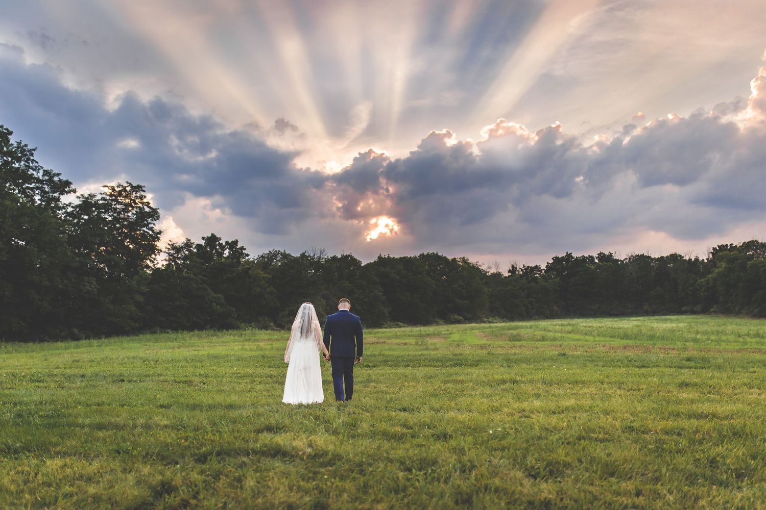Dramatic sky with sunbeams creates silhouette of couple in meadow.
