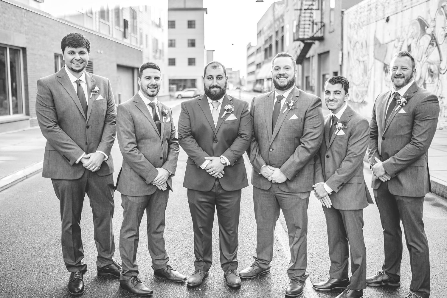 Groomsmen in matching gray suits pose casually on city street.