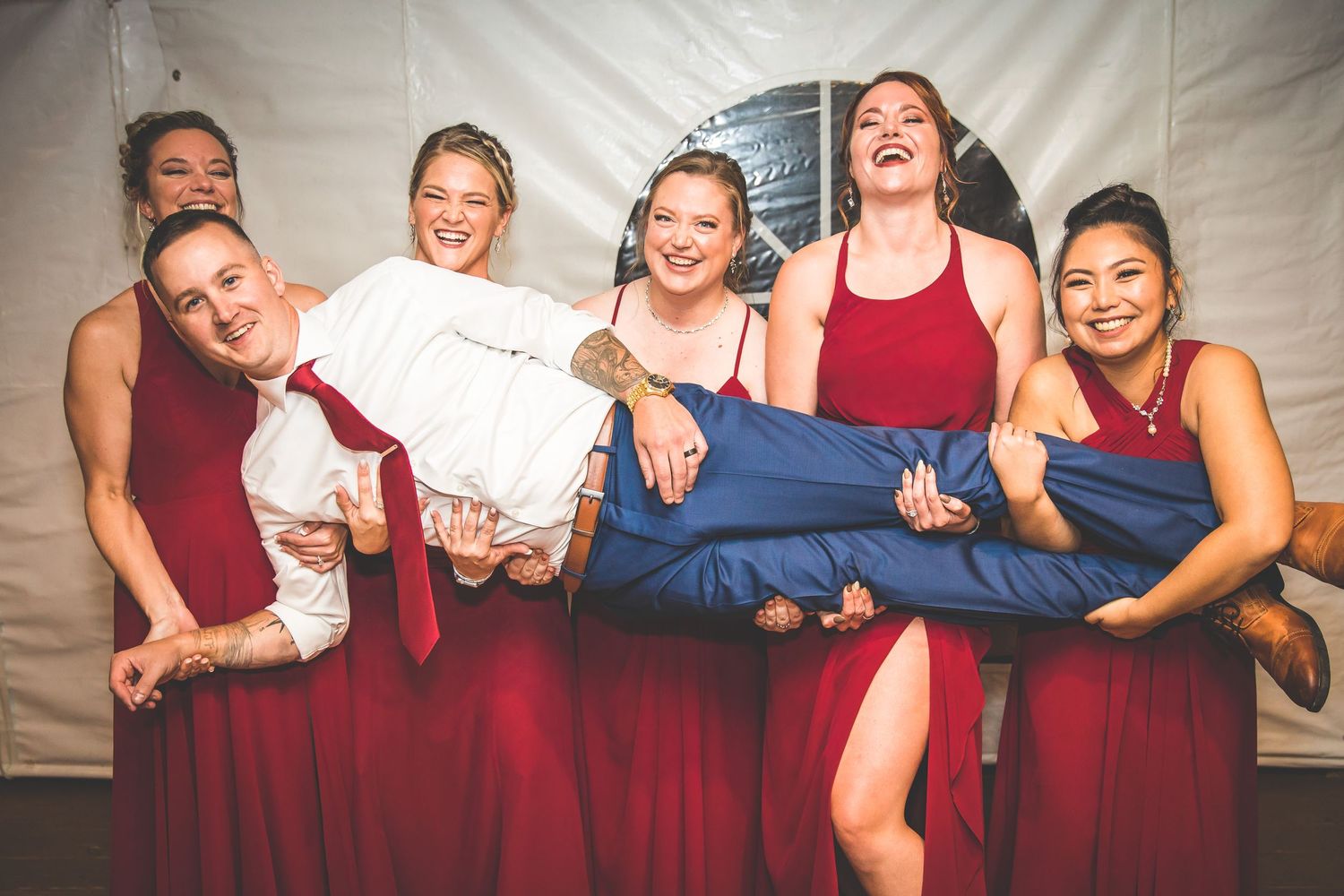 Wedding party posing together on white backdrop wearing burgundy and navy attire.