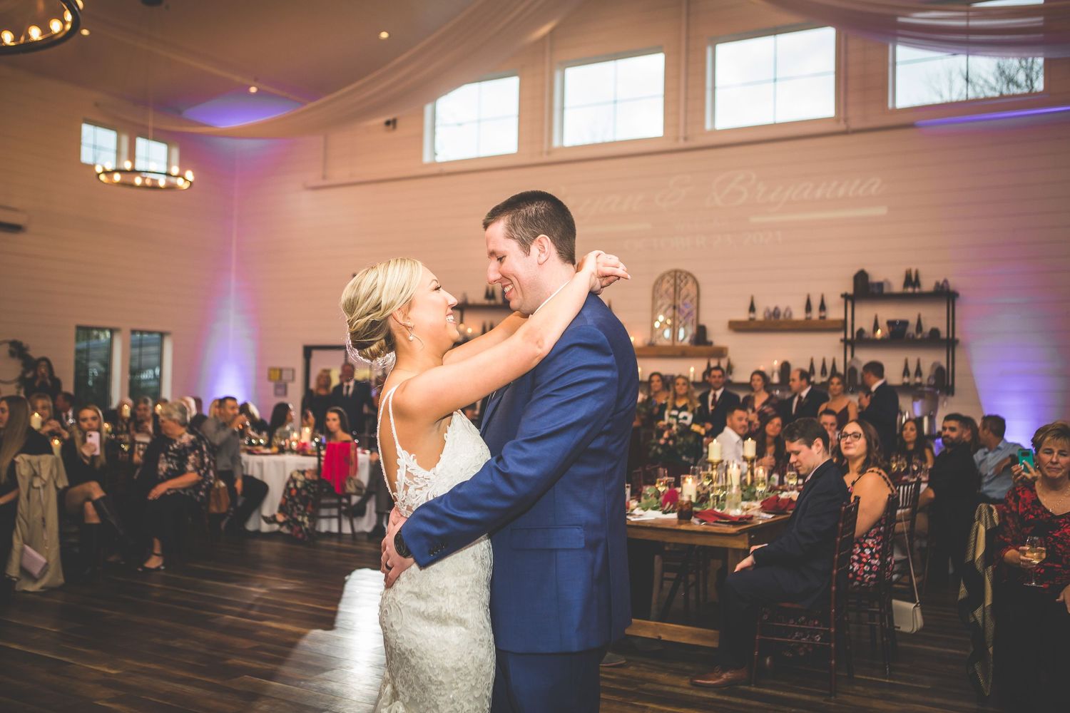 Wedding reception celebration with guests dancing and dining in a spacious venue with blue accent lighting.