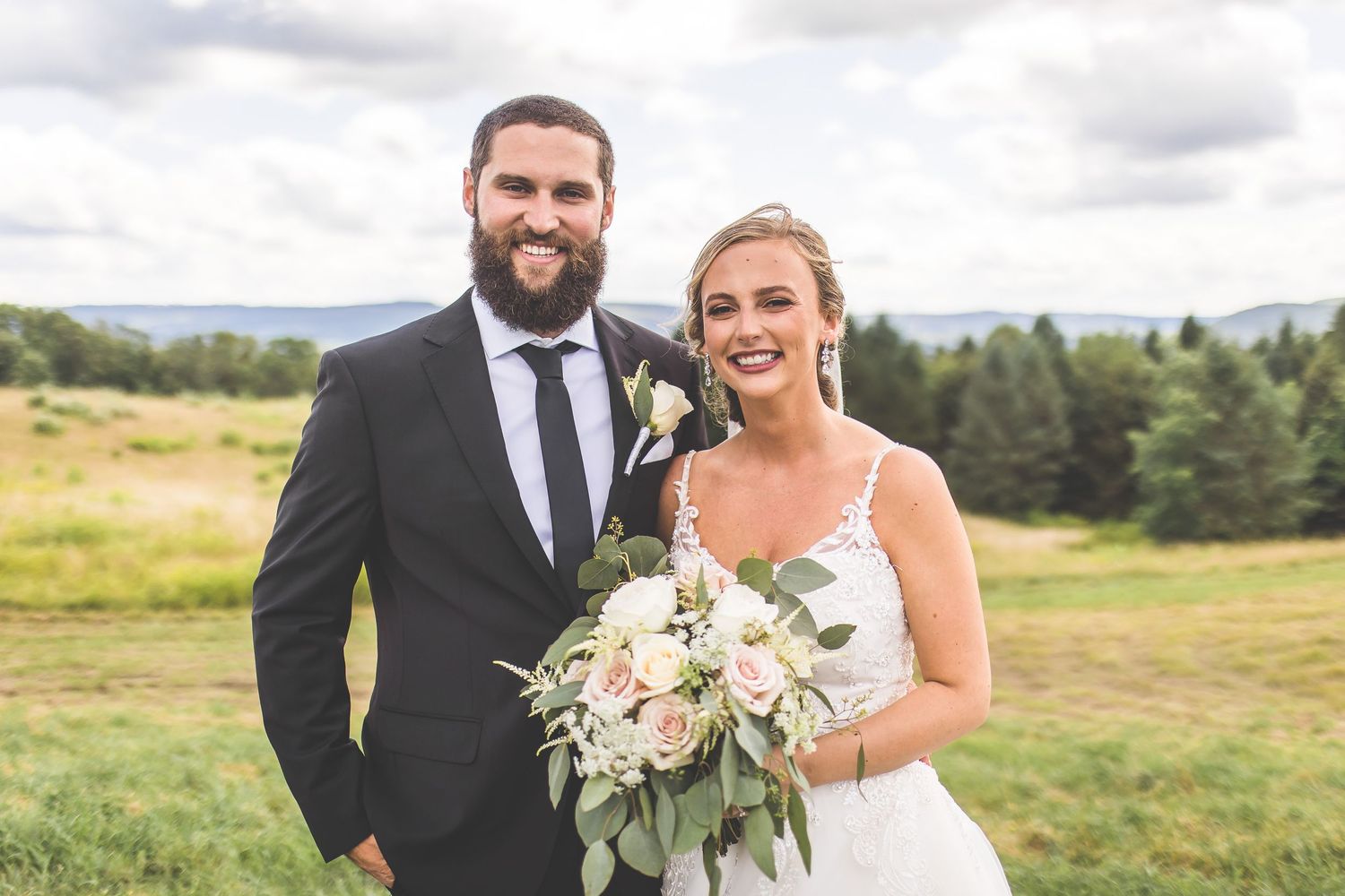 A wedding portrait of a couple standing in a mountain field with white floral bouquet.