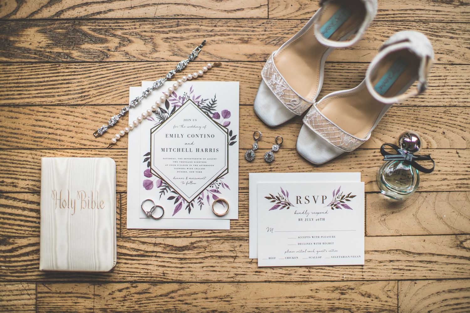 Wedding invitation suite with floral designs displayed on rustic wooden background.