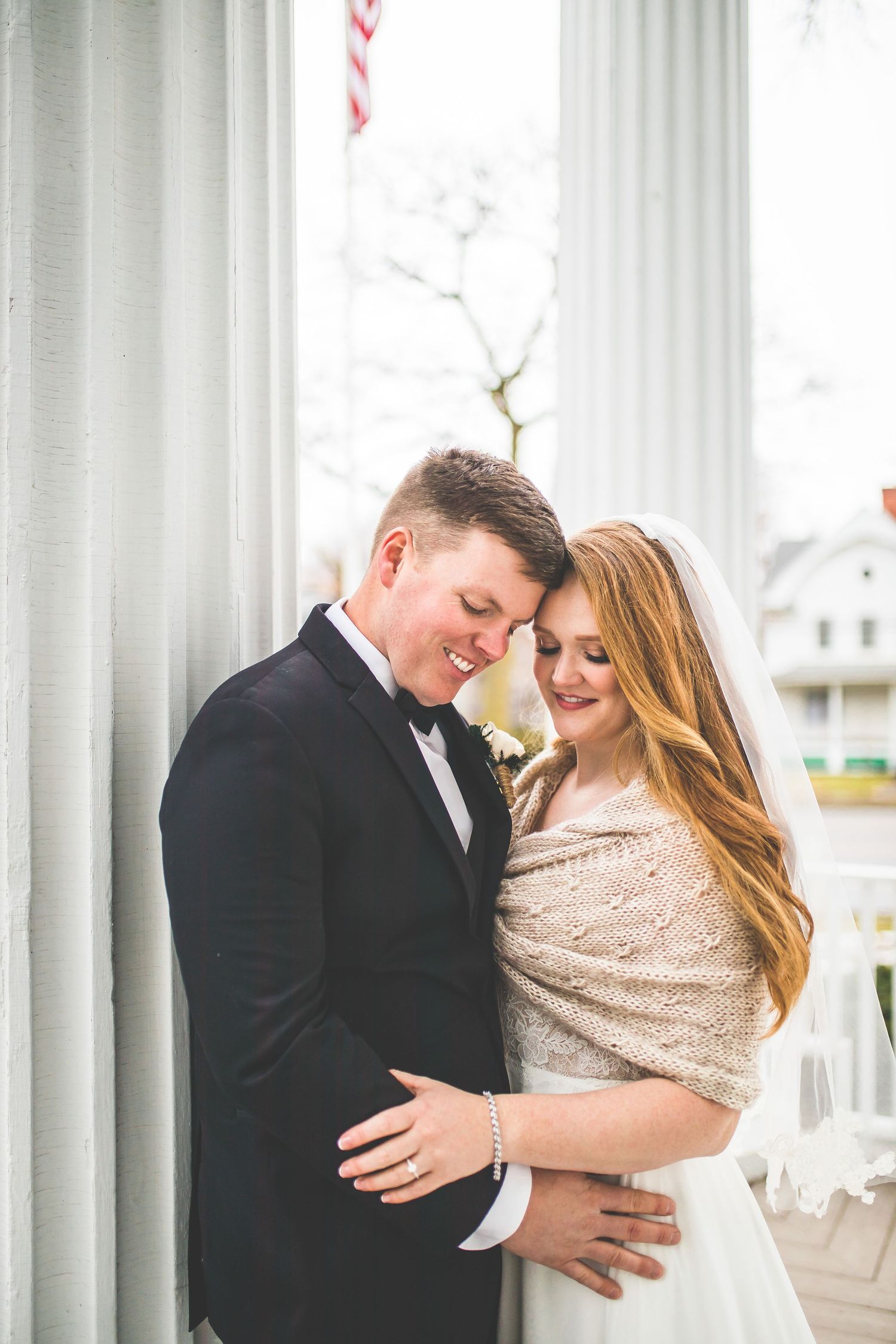 Couple embraces intimately on white columned porch wearing formal wedding attire.