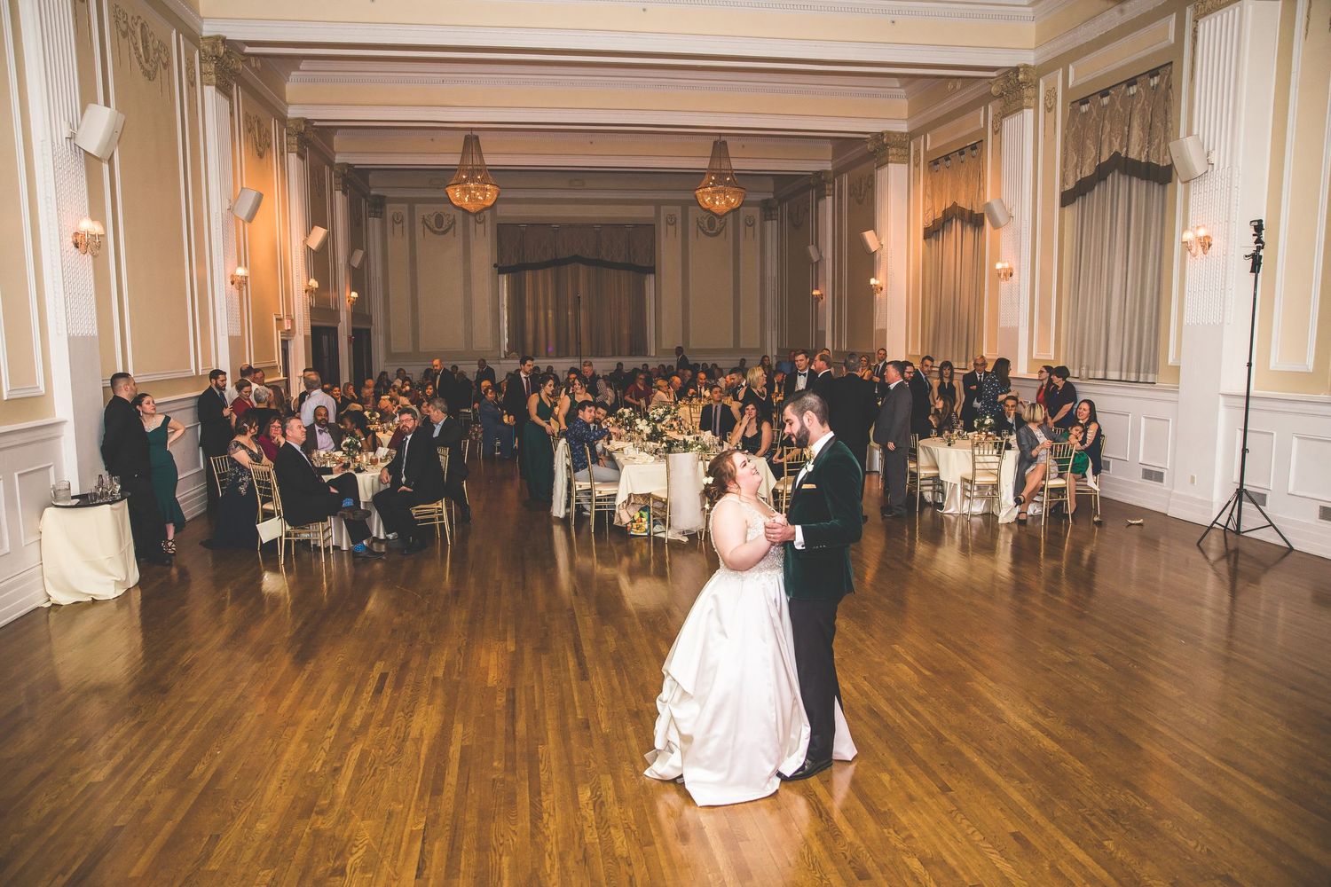 Wedding guests celebrate on a grand ballroom dance floor with warm lighting and elegant decor.