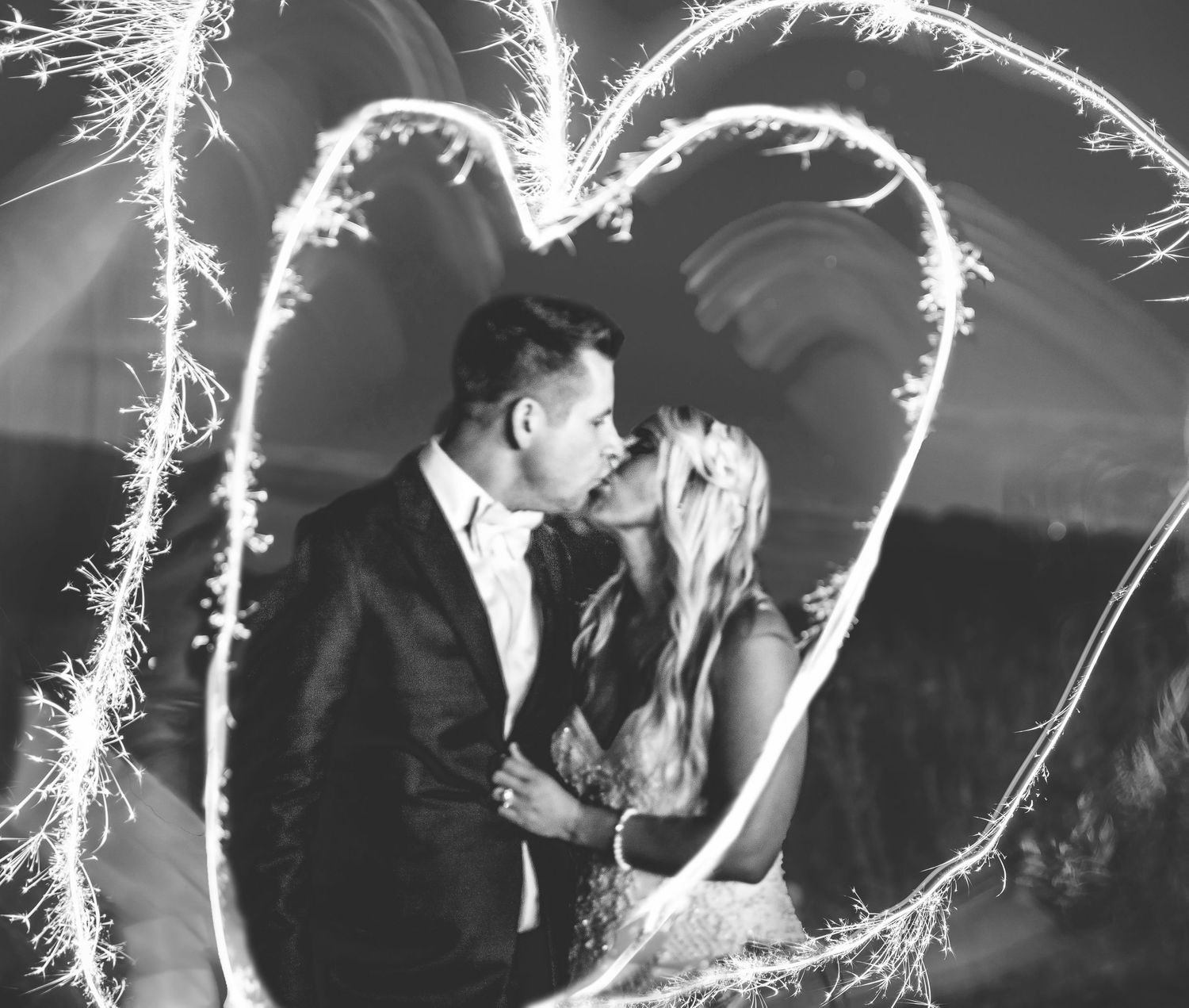 Wedding guests dance surrounded by sparklers creating magical light trails in black and white.