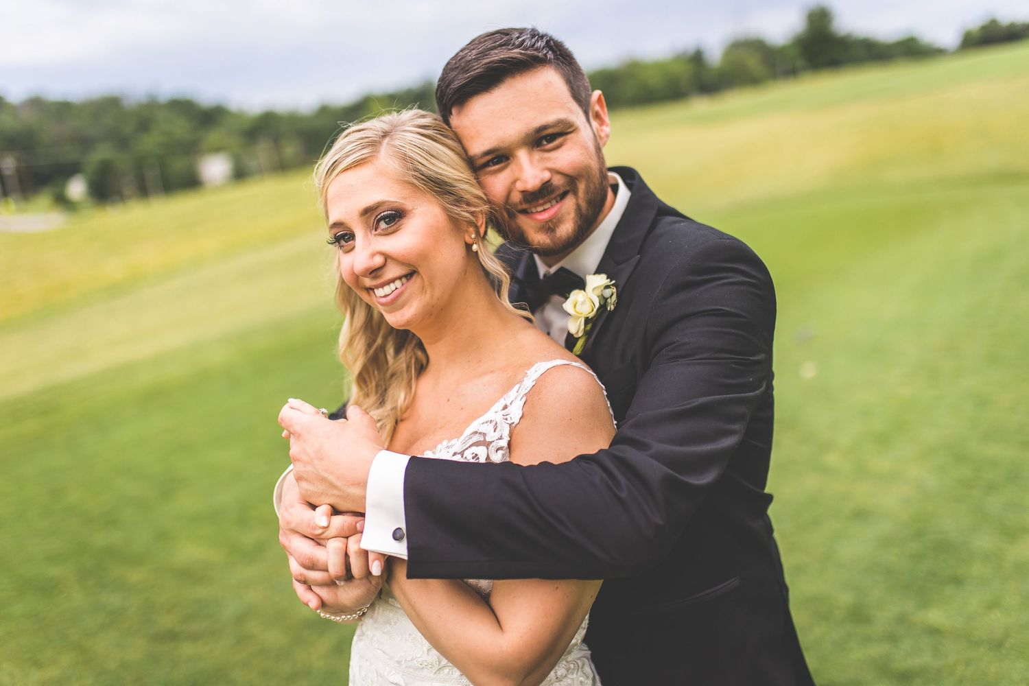 A joyful wedding couple laughs together while posing on a manicured golf course.