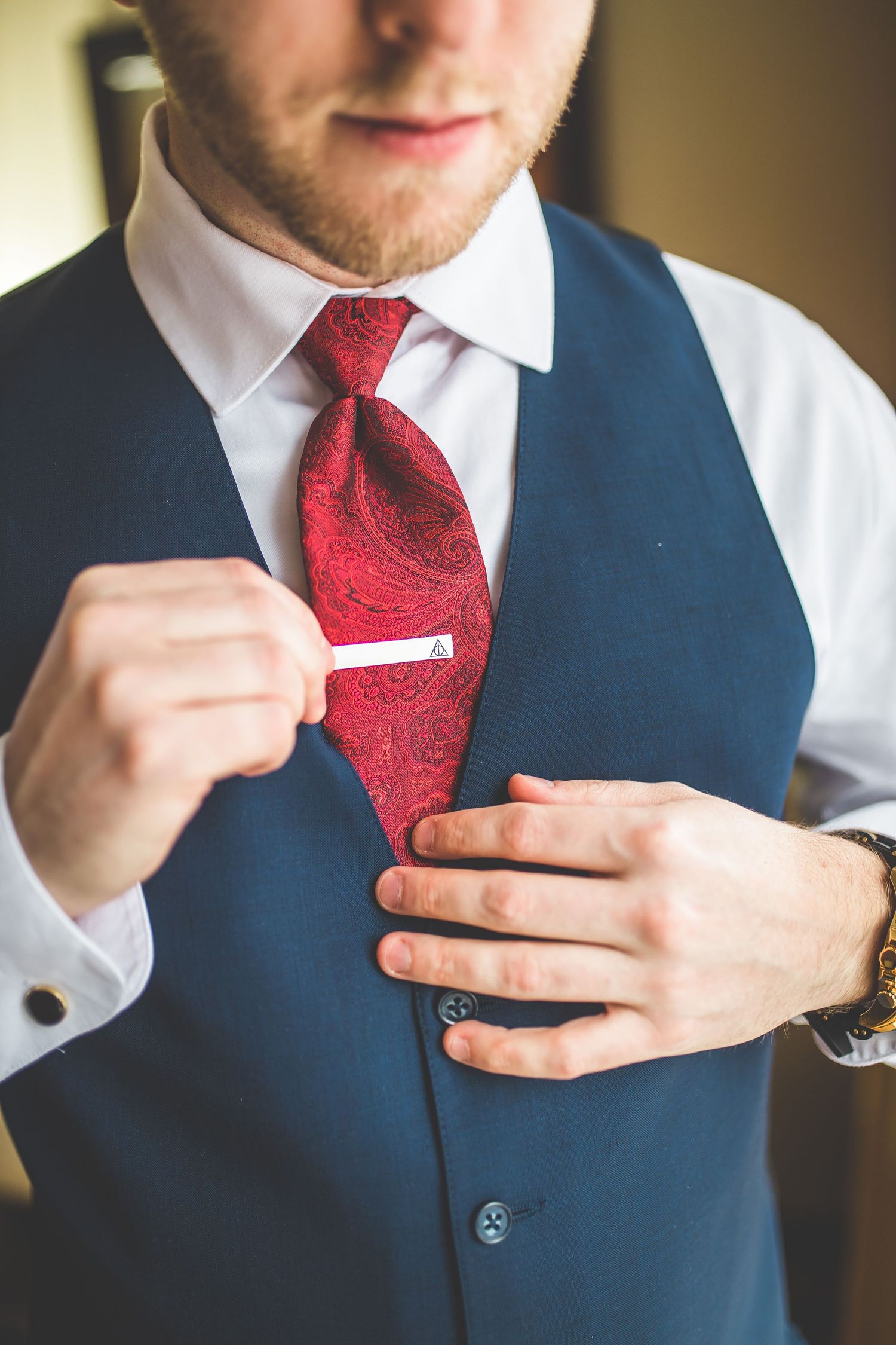 Close-up of blue vest and red tie with silver tie clip being adjusted.