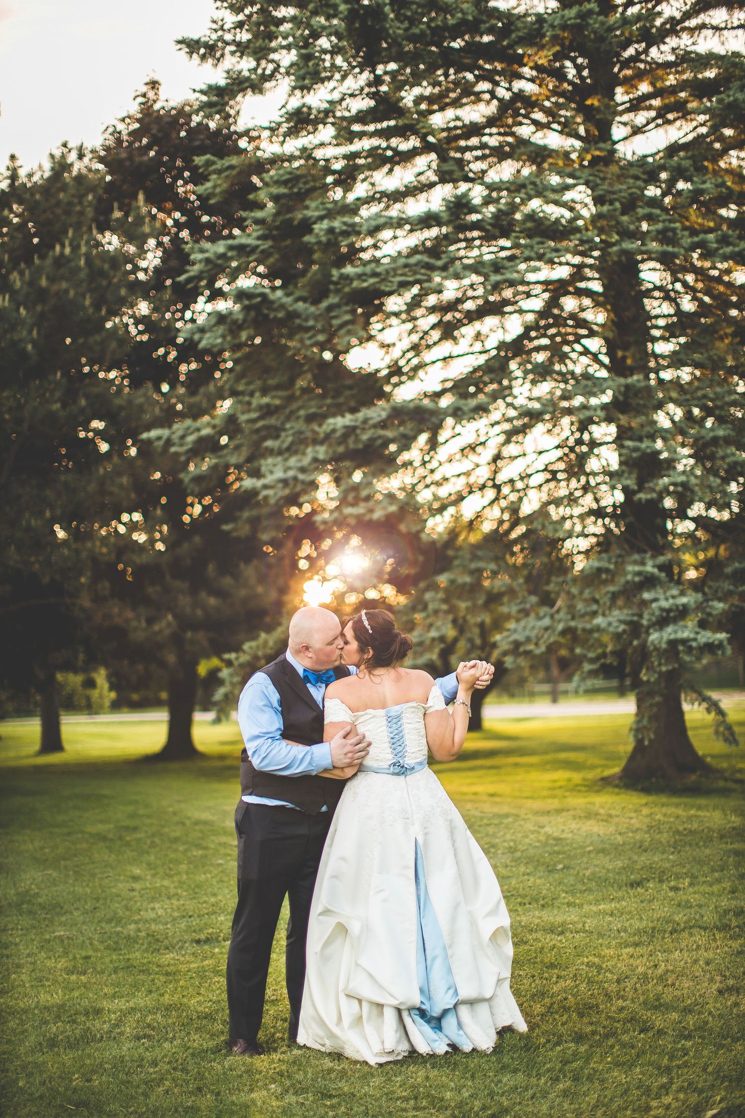 Couple dancing together in a sunlit garden with evergreen trees during golden hour.