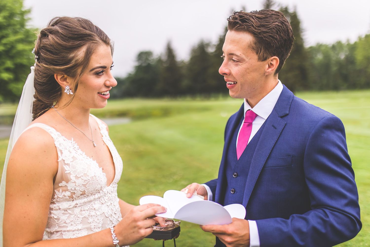 A couple shares a lighthearted moment while exchanging written vows in an outdoor setting.