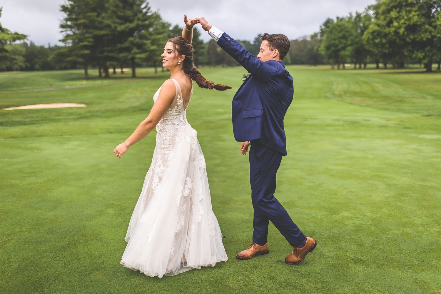 Couple sharing playful dance moves on a sunny golf course during their wedding day.