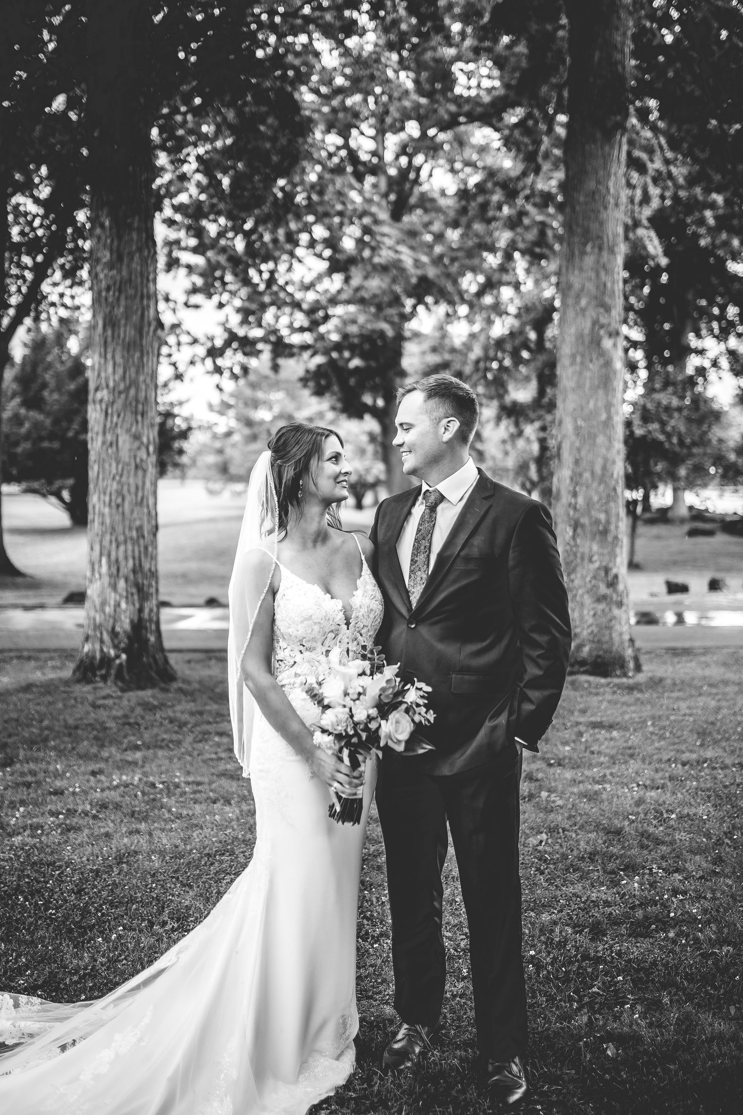 Black and white romantic wedding portraits captured under mature trees in a park.