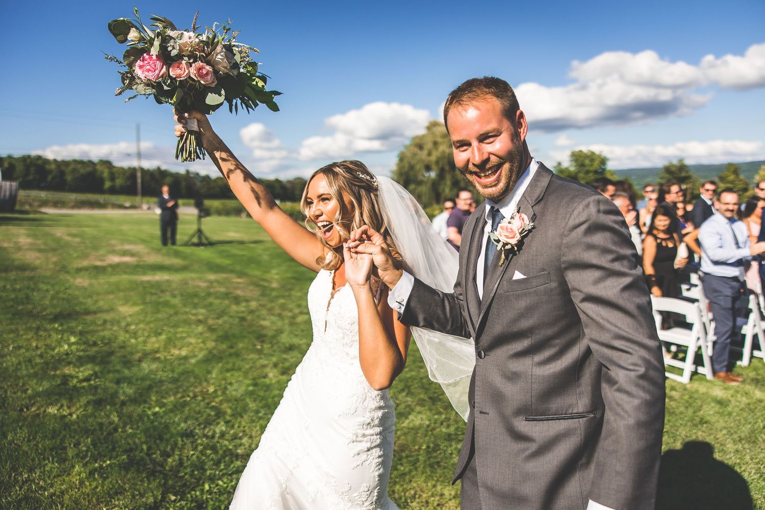 Wedding party celebrates with joyful dance moves during outdoor reception at scenic vineyard.