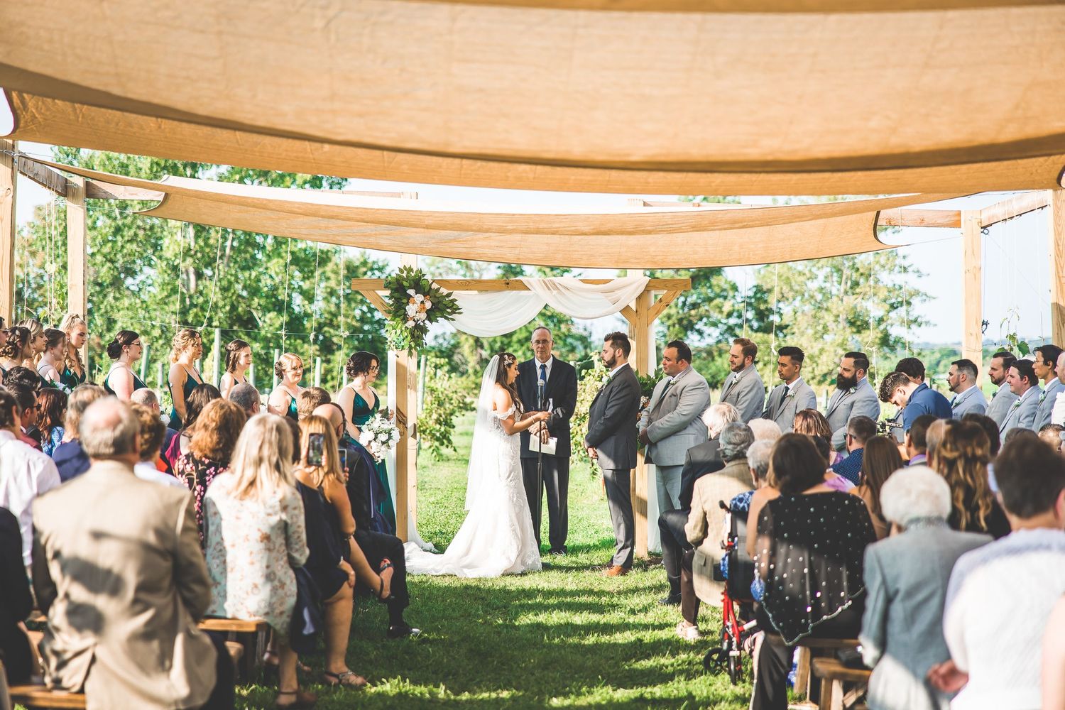 Wide view of outdoor wedding ceremony with guests seated under a canopy tent.