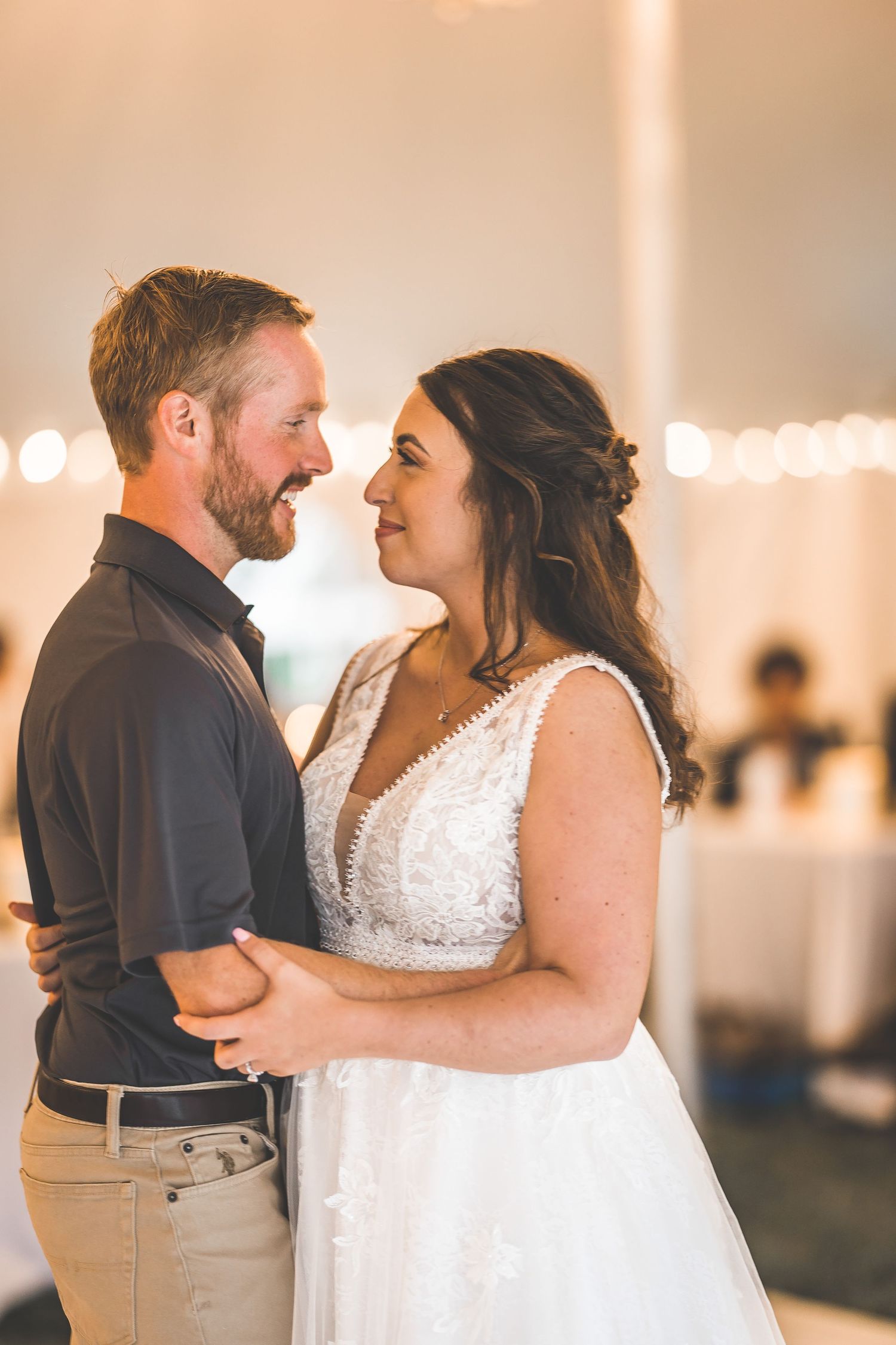 A couple shares a romantic first dance moment at their wedding reception under twinkling lights.