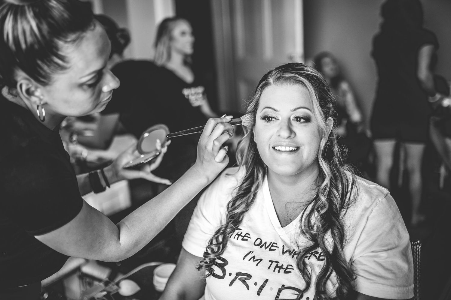 Wedding day preparation scene with makeup being applied in black and white.