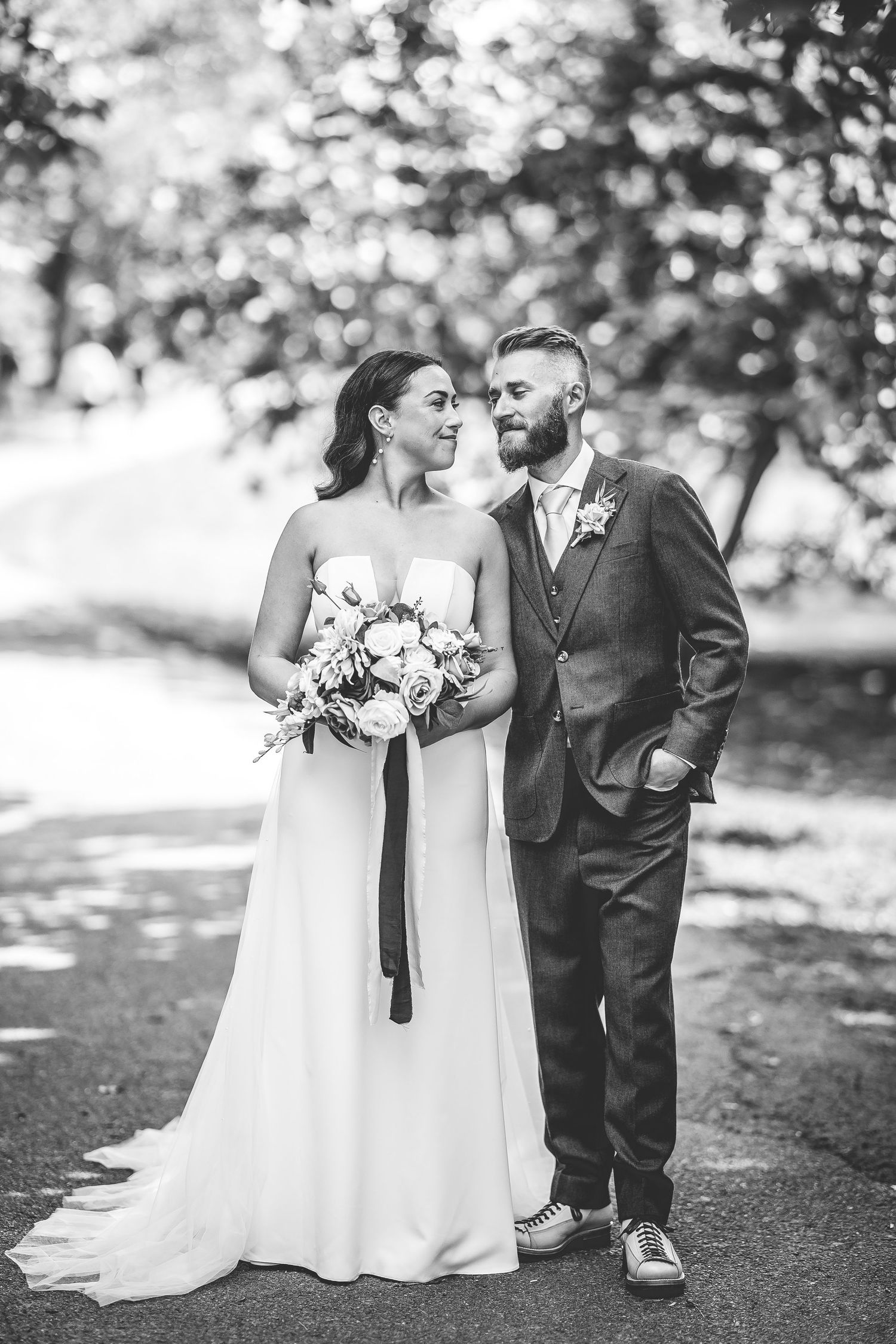 Black and white portrait of couple in wedding attire on garden path.