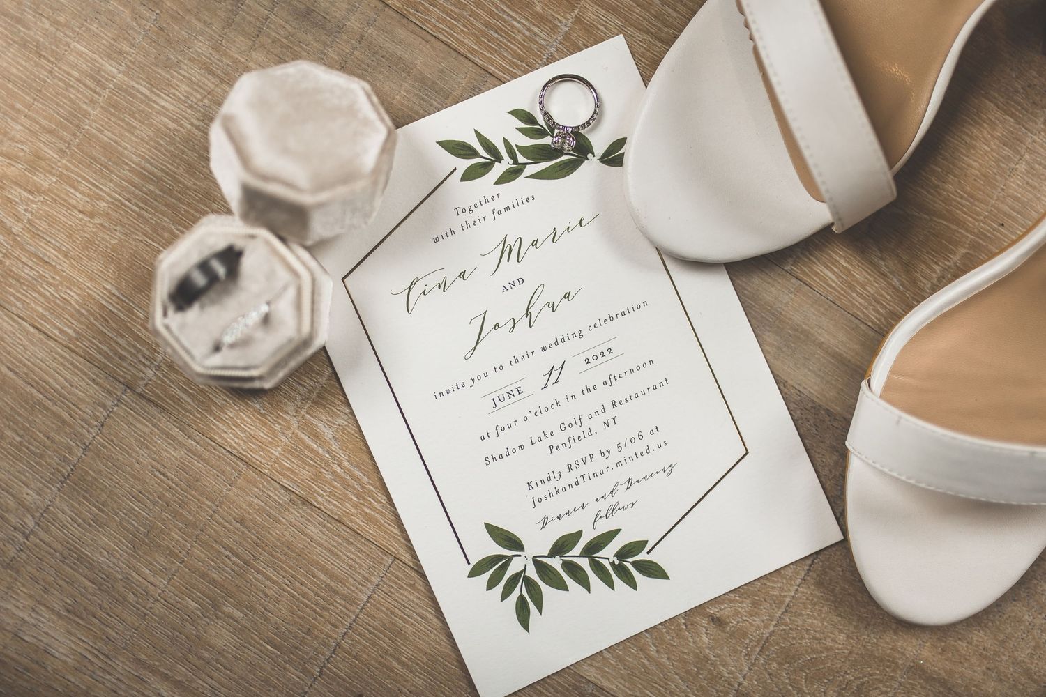 Wedding invitation with elegant greenery details and white shoes on rustic wooden background.