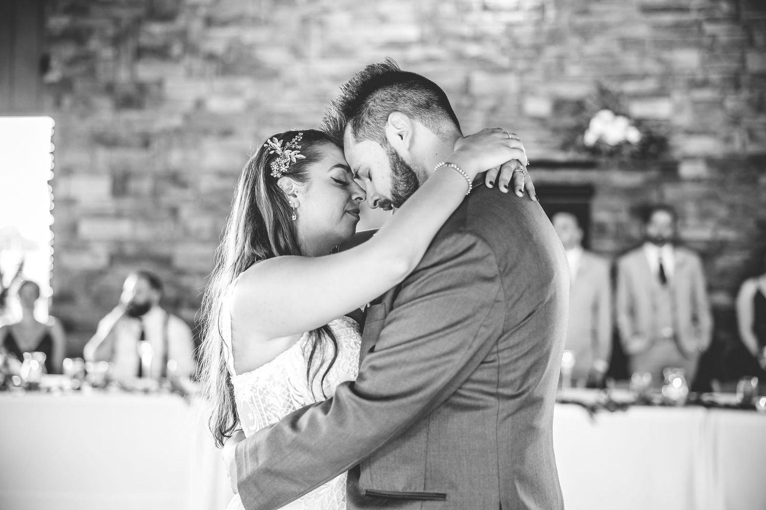 A couple shares their first dance at a wedding reception in front of a stone wall backdrop.