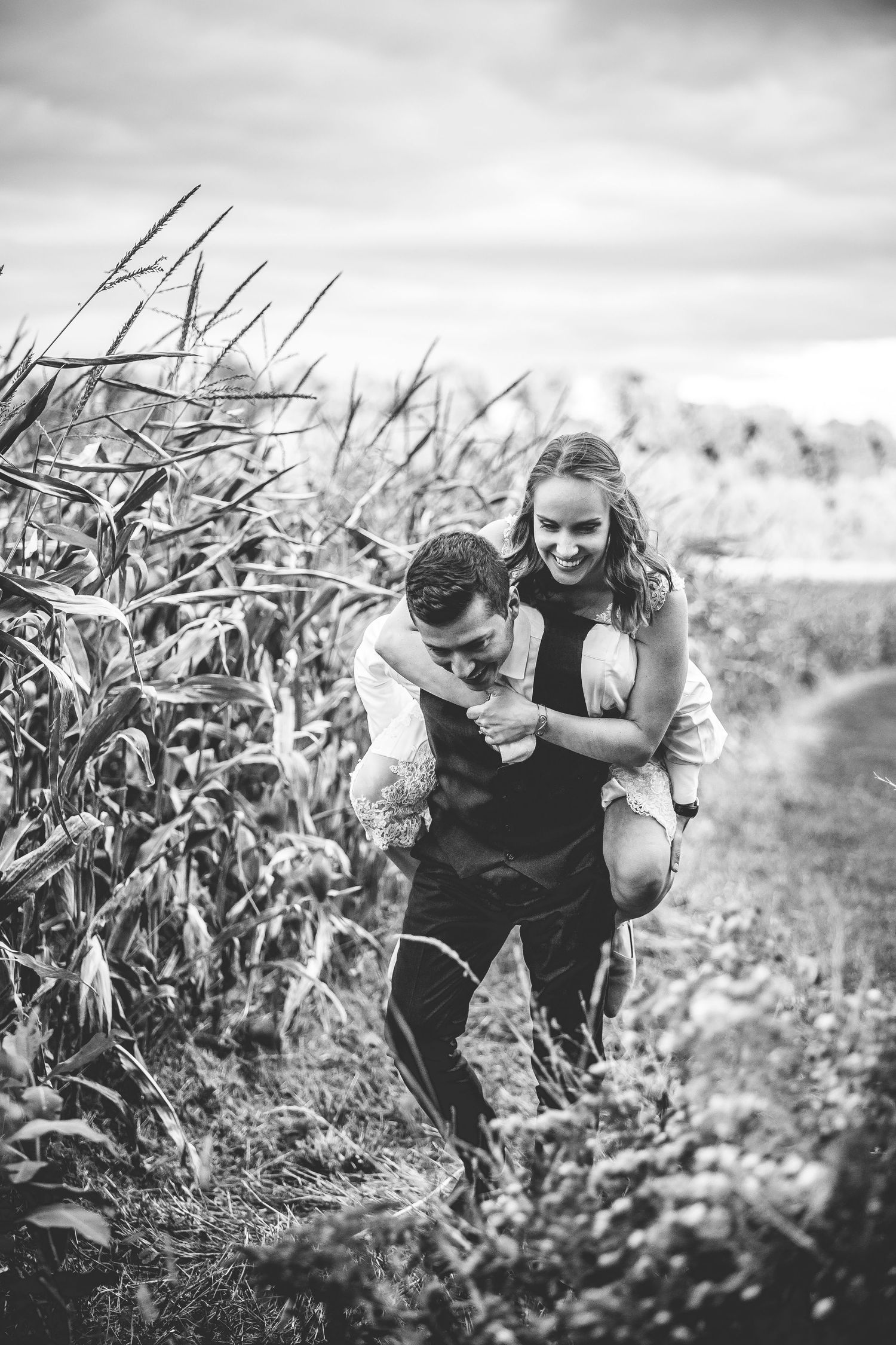 Black and white photo of playful piggyback ride along cornfield path.