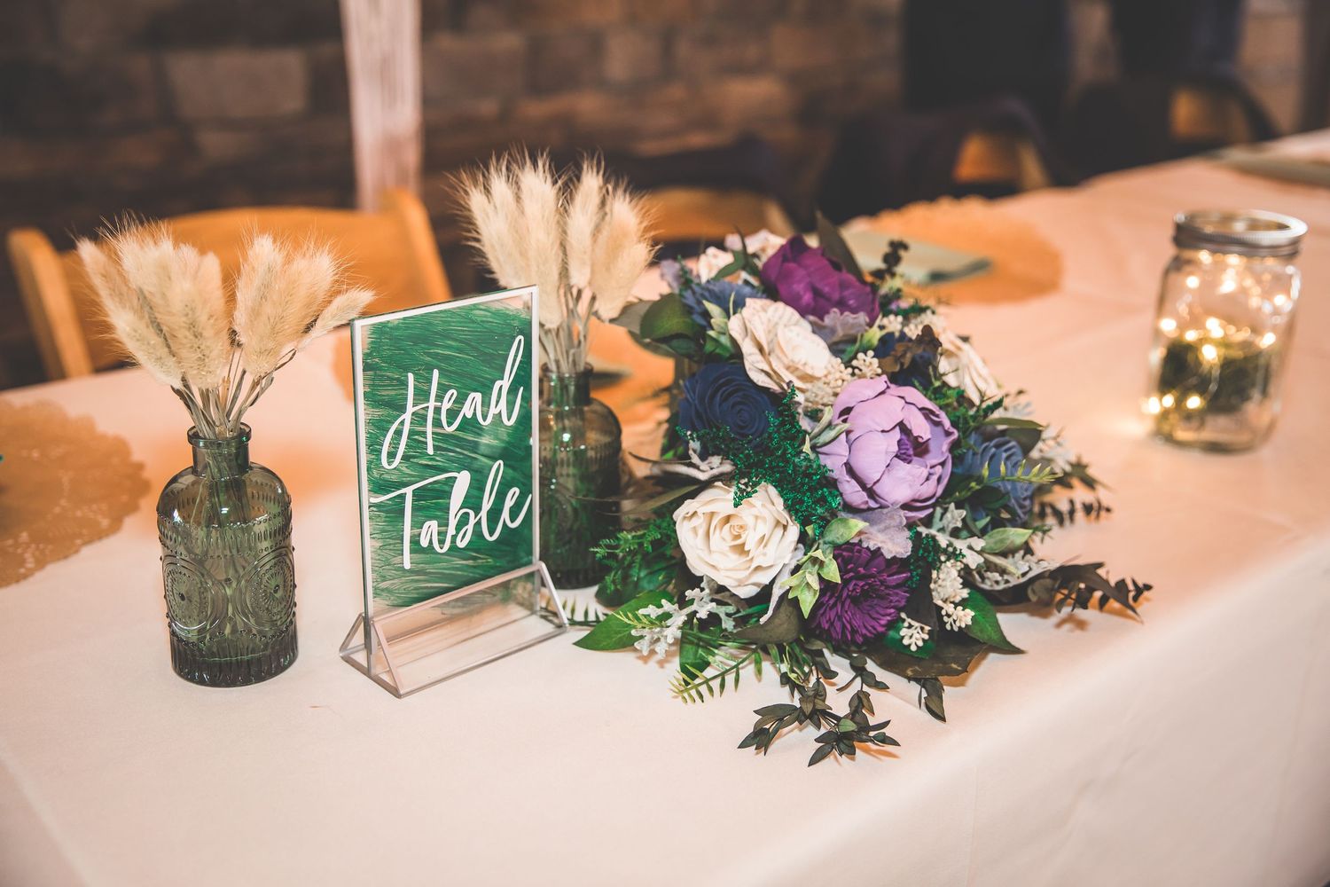 Wedding reception table decorated with purple and white floral centerpieces and chalkboard signs.