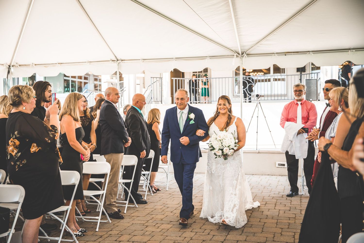 Wide view of wedding ceremony under white tent with guests seated in rows.
